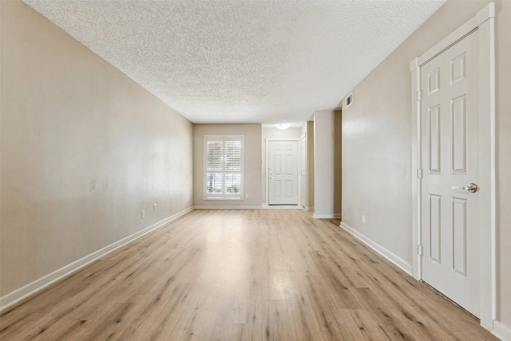 Wood-finish flooring, neutral wall tones, window with blinds, white trim, and a paneled interior door