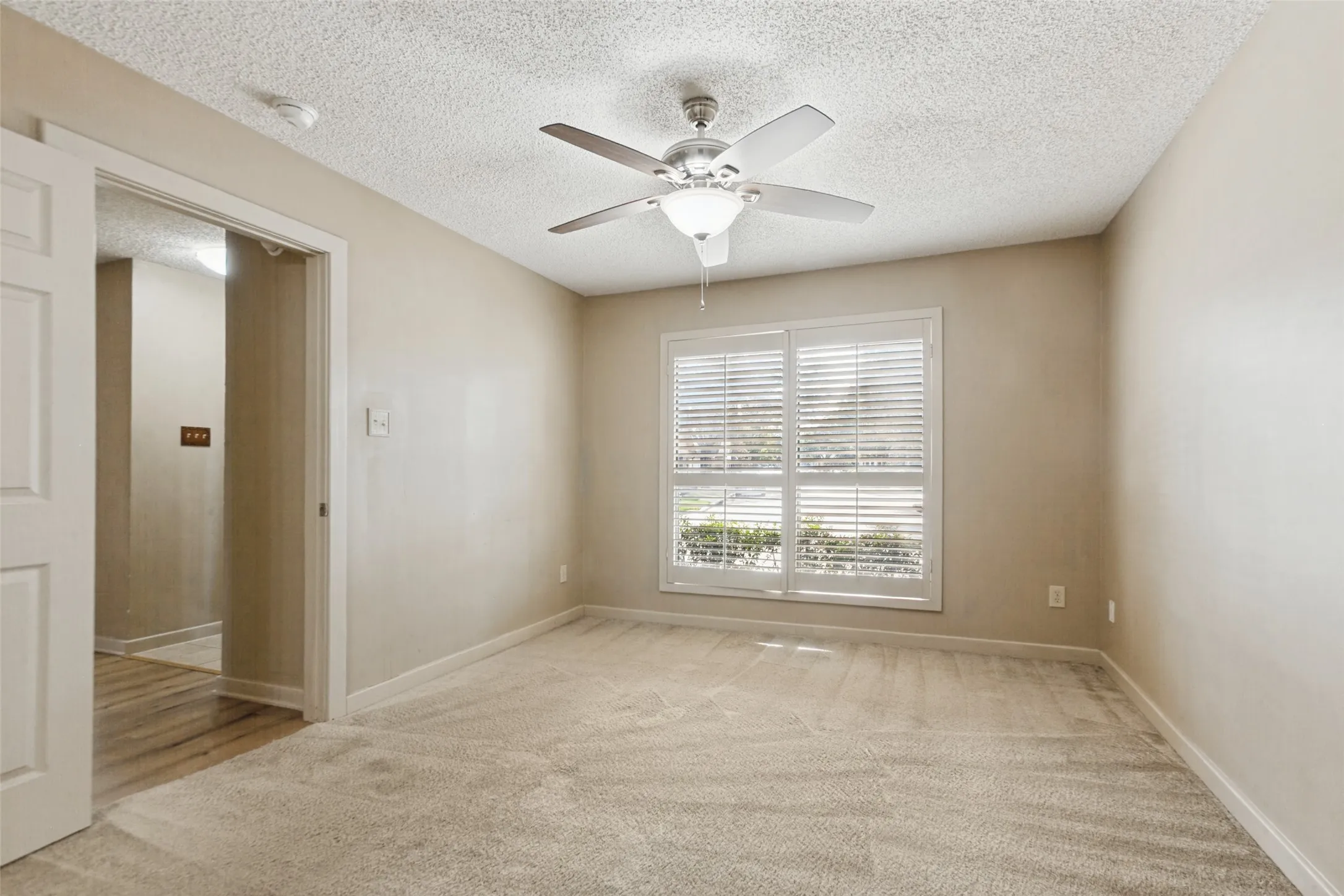Neutral-toned walls with textured ceiling, carpeted flooring, and a ceiling fan with integrated lighting