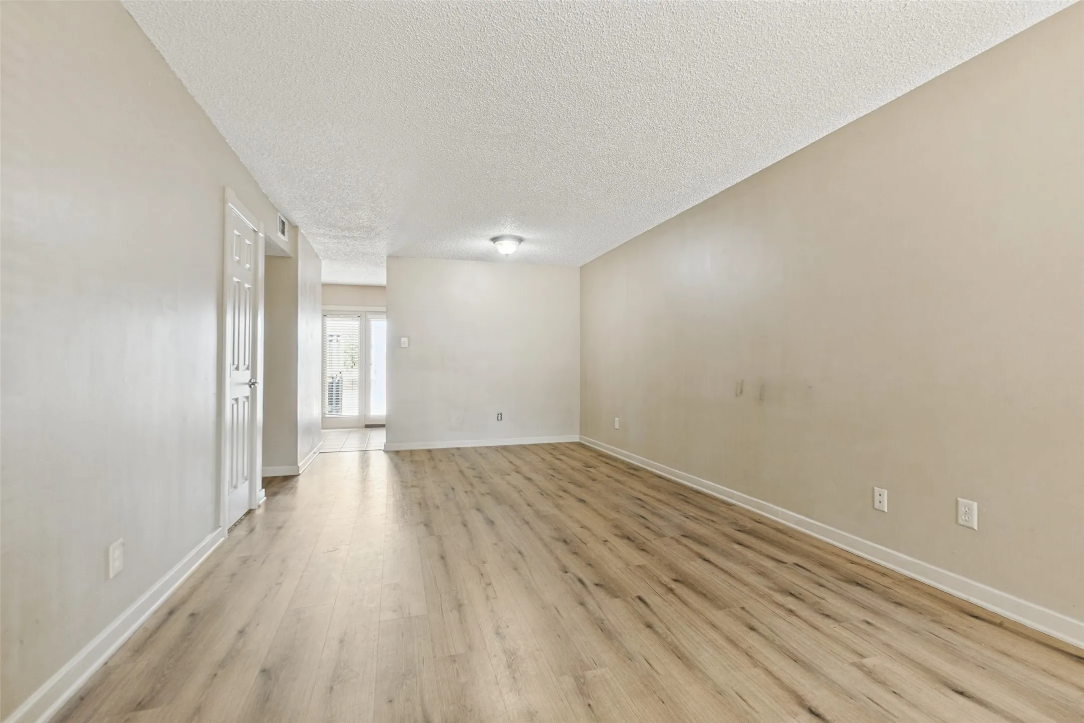 Spacious room with wood-finish flooring, light-colored walls, white trim, and a ceiling-mounted light fixture