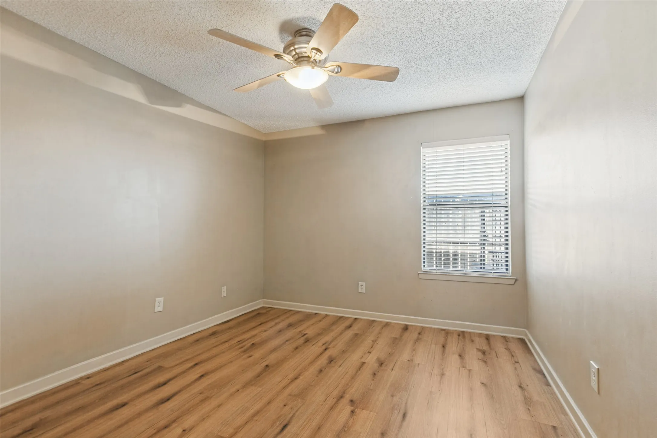 Wood-finish flooring, ceiling fan with integrated lighting, window with blinds, and tray ceiling detailing