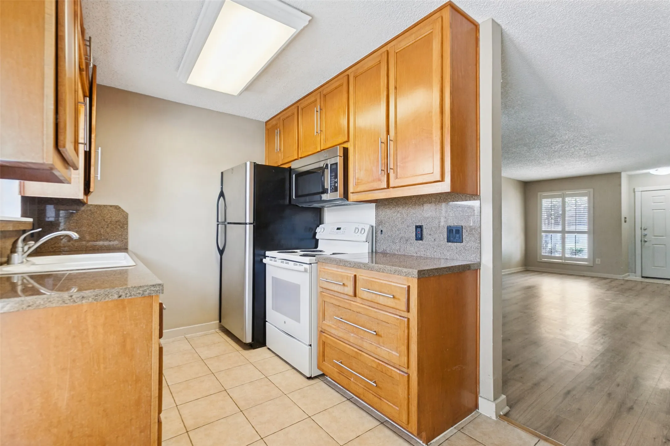 Kitchen featuring wood cabinetry, stone countertops, tile flooring, stainless steel refrigerator, and integrated sink