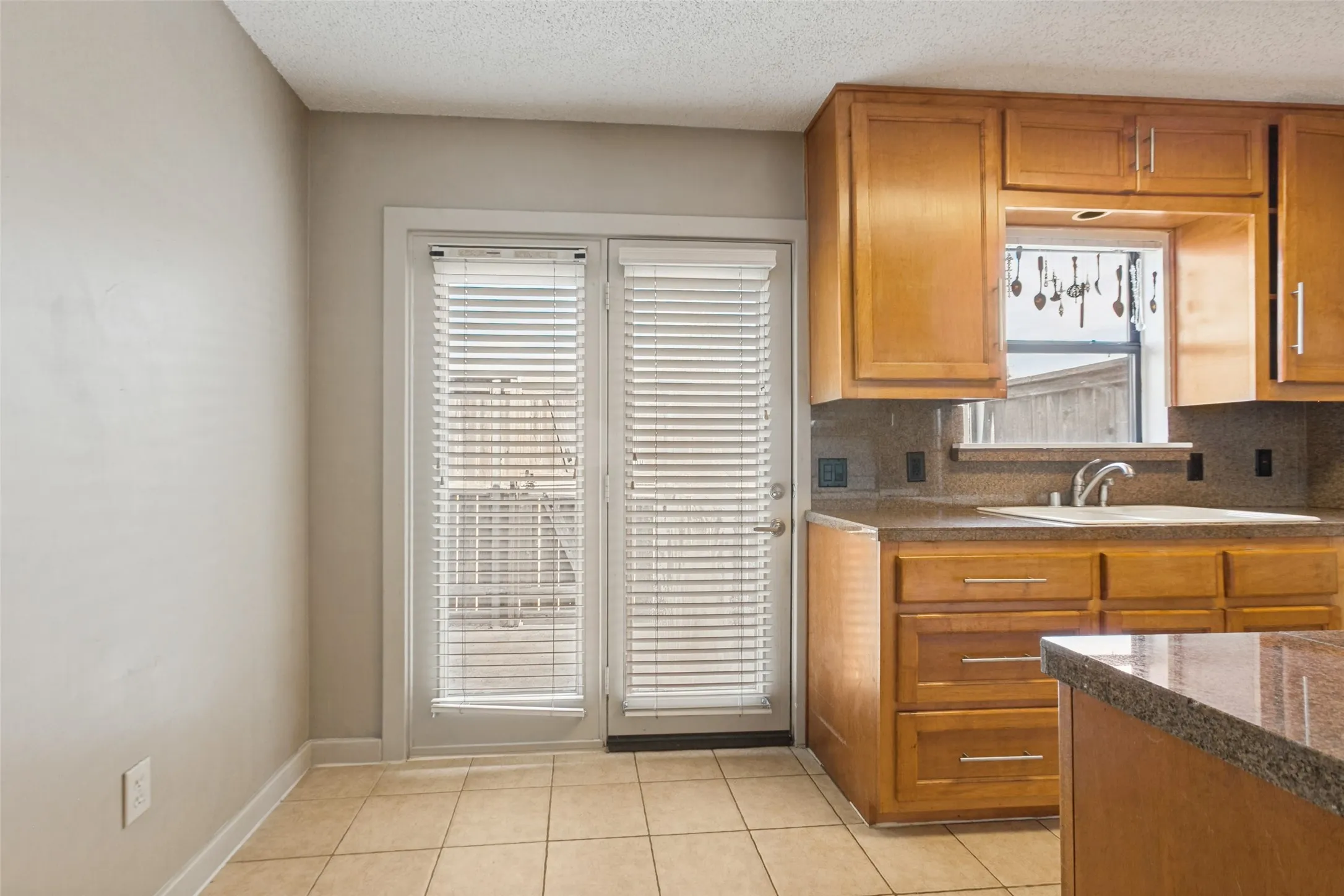 Warm wood cabinetry with brushed nickel hardware, granite-look countertops, and a stainless steel sink with a gooseneck faucet