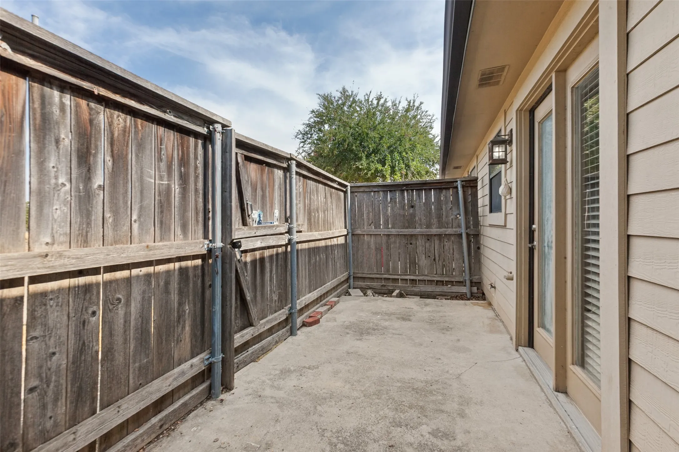 Private patio with concrete flooring, wood privacy fencing, and exterior wall lighting