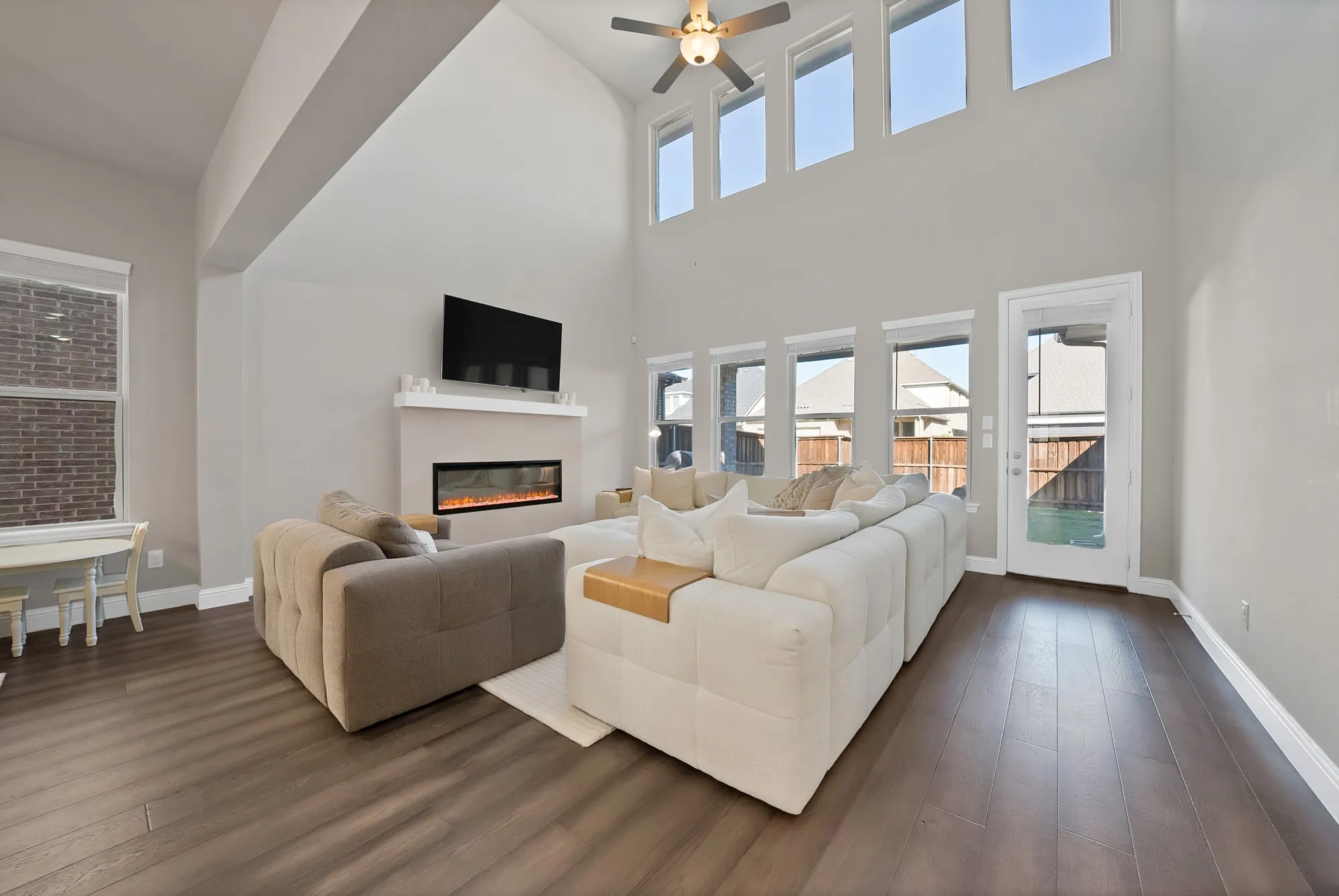 Soaring ceilings, wood-finish flooring, an electric fireplace, multiple windows, and a ceiling fan