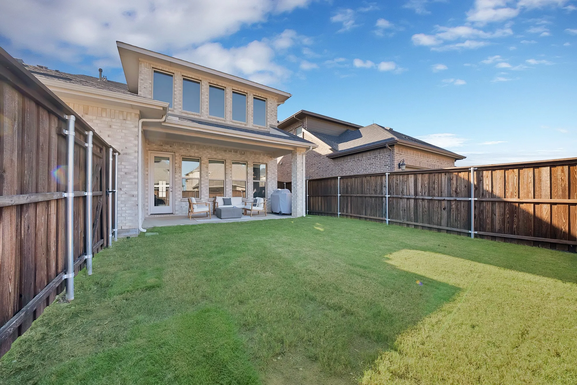 Expansive backyard with a covered patio, brick exterior, and a second-story dormer featuring a row of windows