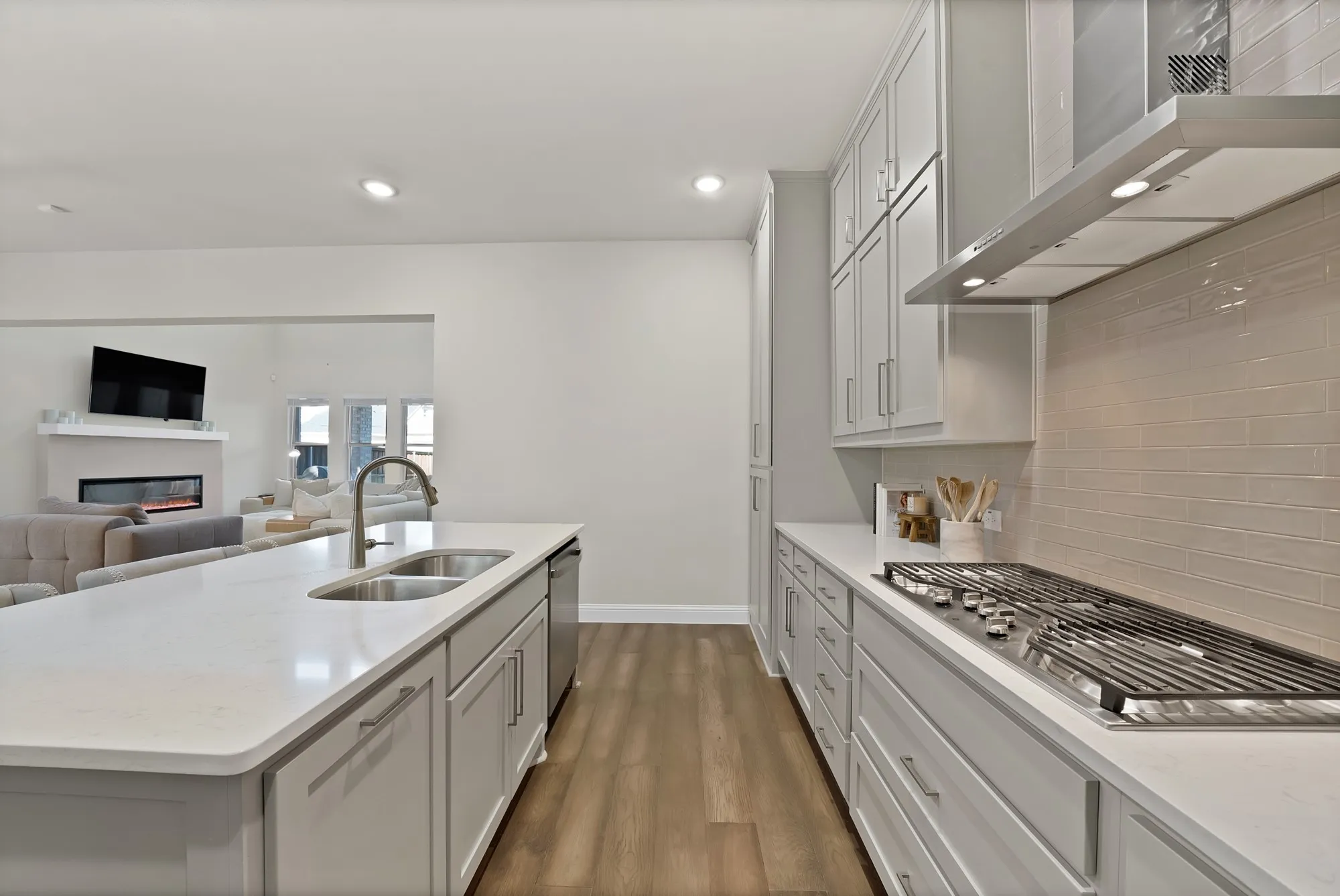 Modern kitchen featuring light gray cabinetry, stainless steel appliances, a white countertop island with a double basin sink, and wood-finish flooring