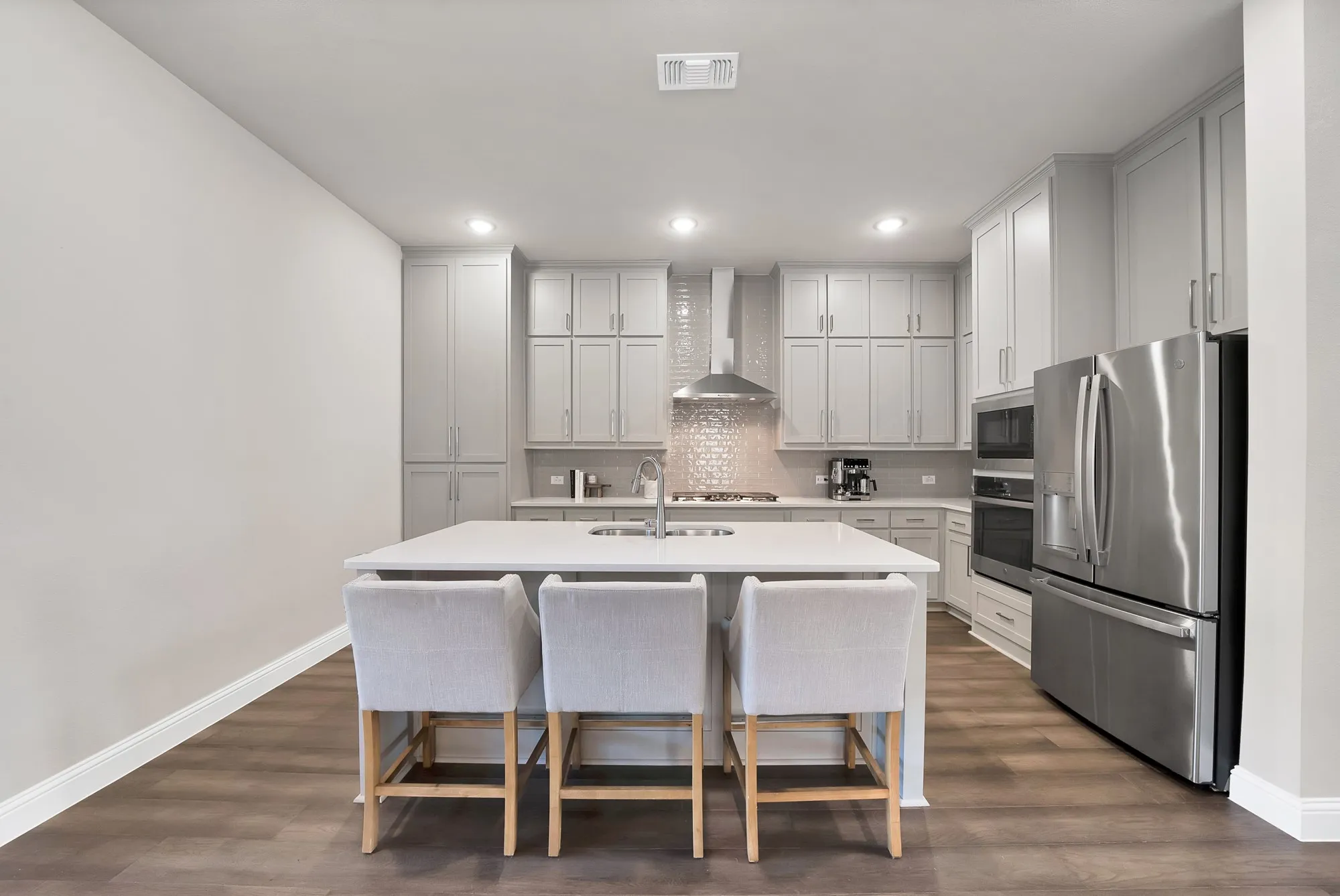 Contemporary kitchen featuring wood-finish flooring, light-colored cabinetry, a central island with an integrated sink, stainless steel appliances, and recessed lighting