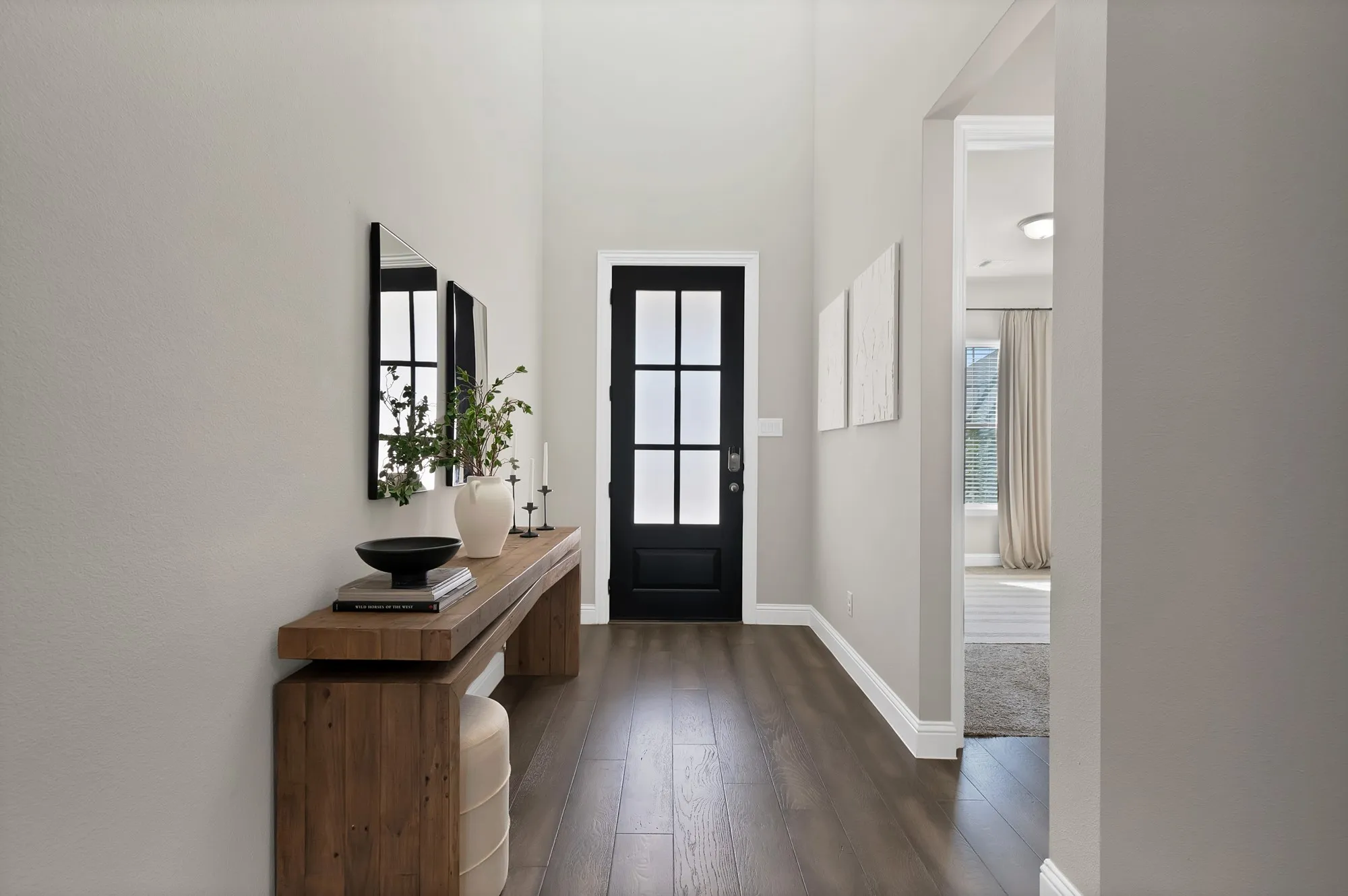 Wood-finish flooring with crisp white trim, a black paneled door, and neutral wall tones