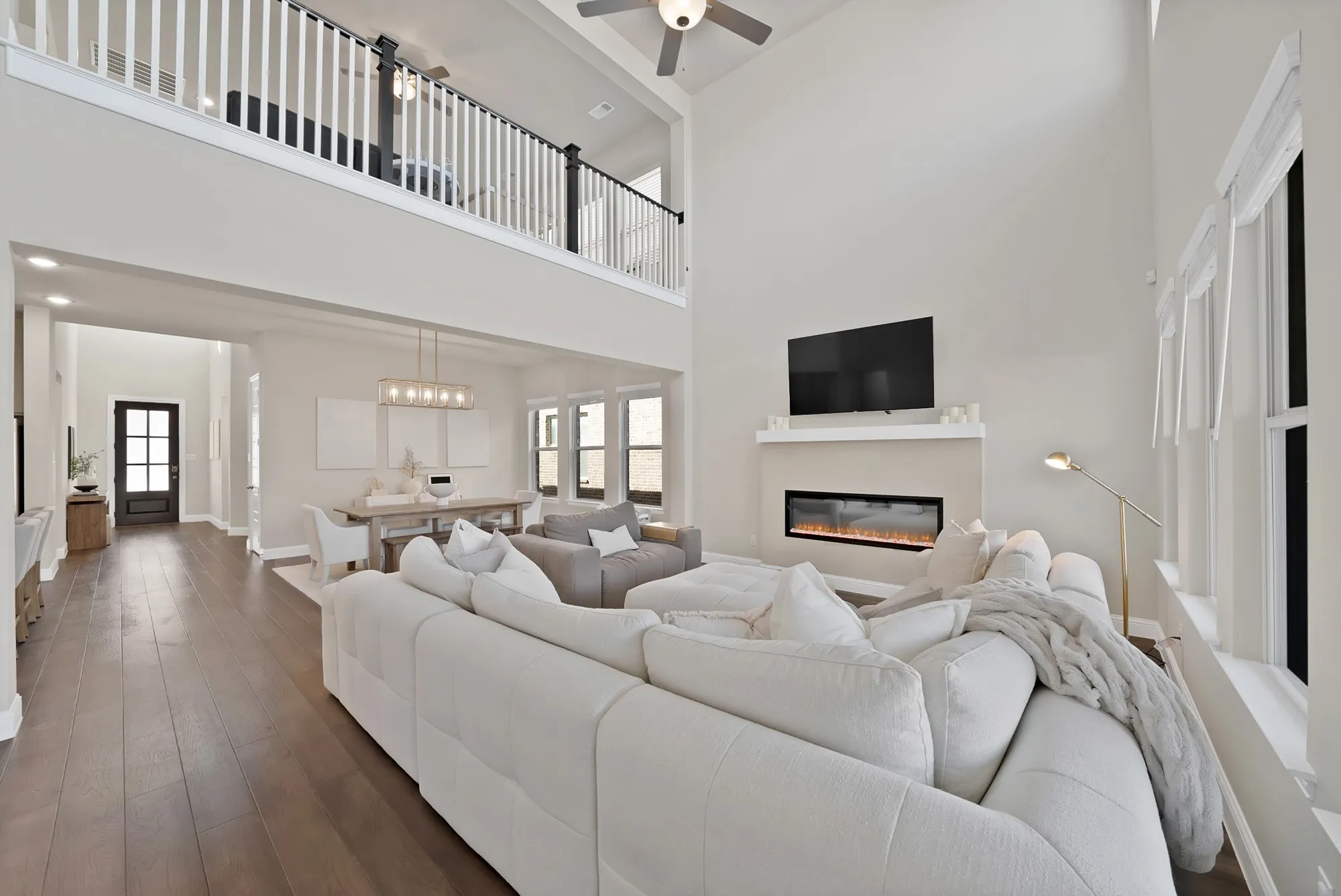 Two-story living area with high ceilings, wood-finish flooring, and an integrated electric fireplace below a mounted television