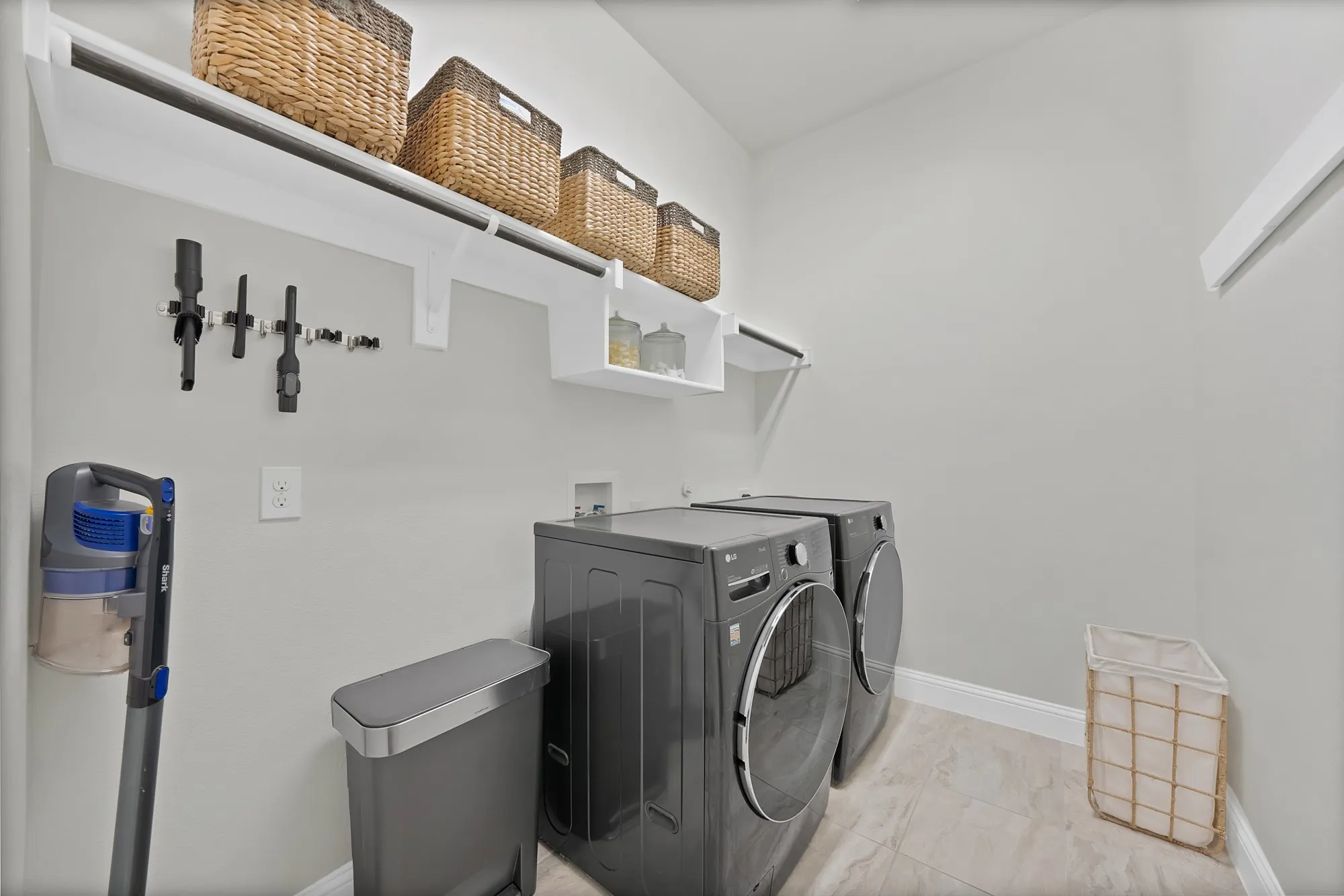 Integrated laundry area featuring neutral-toned walls, tile flooring, and white shelving with a hanging rod