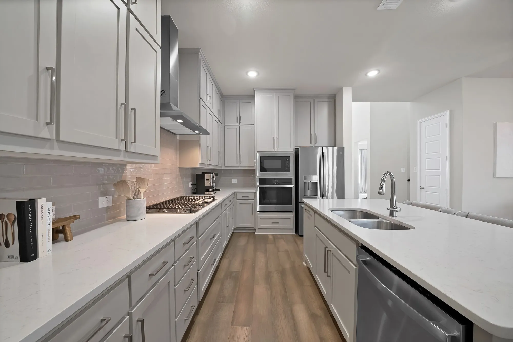Modern kitchen featuring light gray cabinetry, stainless steel appliances, a center island with sink, white countertops, and wood-finish flooring