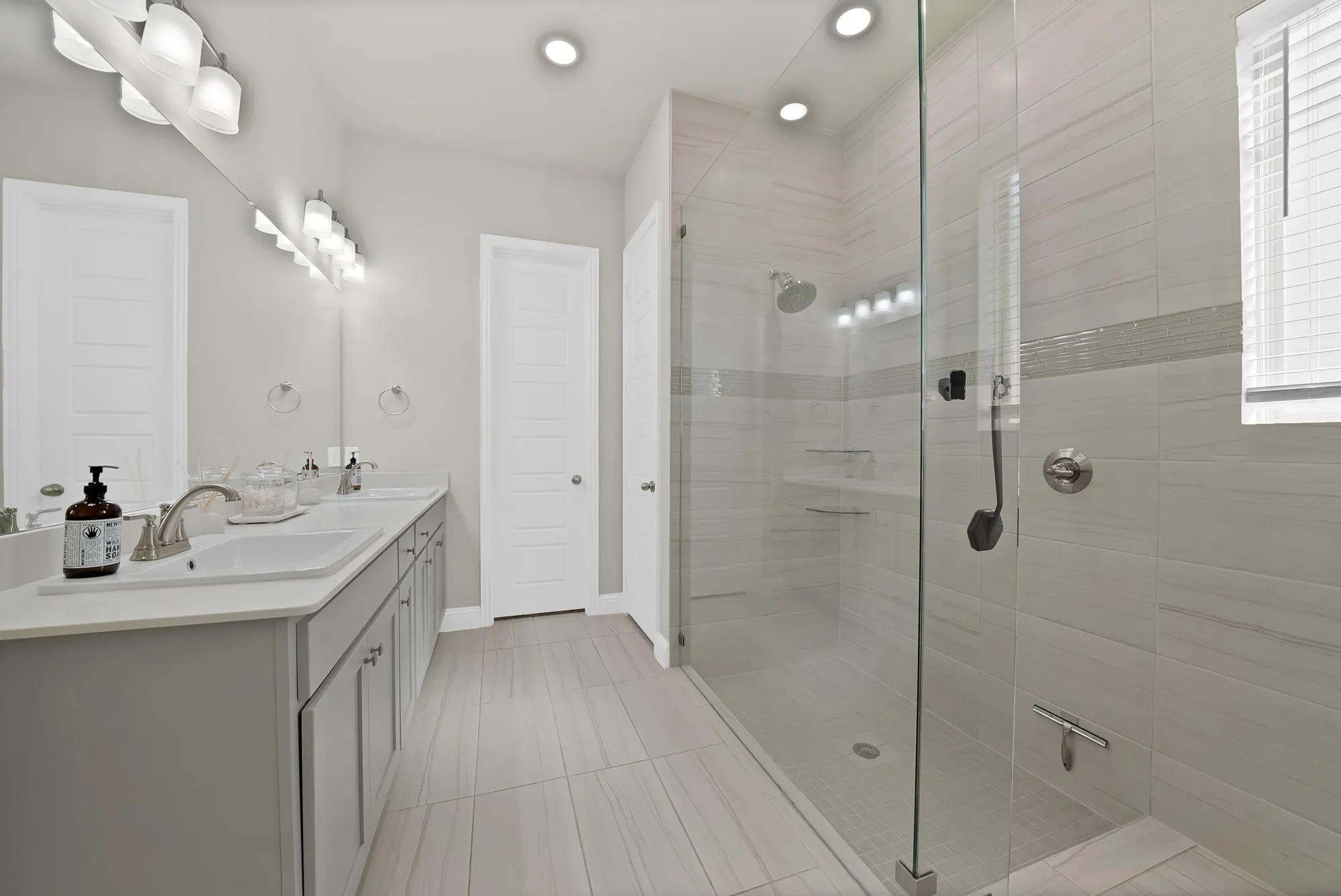Dual vanity with undermount sinks, a spacious walk-in shower with a glass enclosure, light-toned tile flooring, and recessed lighting