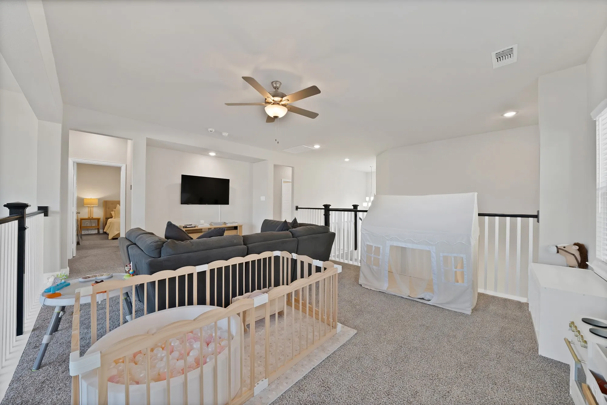 Spacious carpeted upper-level area featuring a ceiling fan, recessed lighting, white walls, and black and white railings