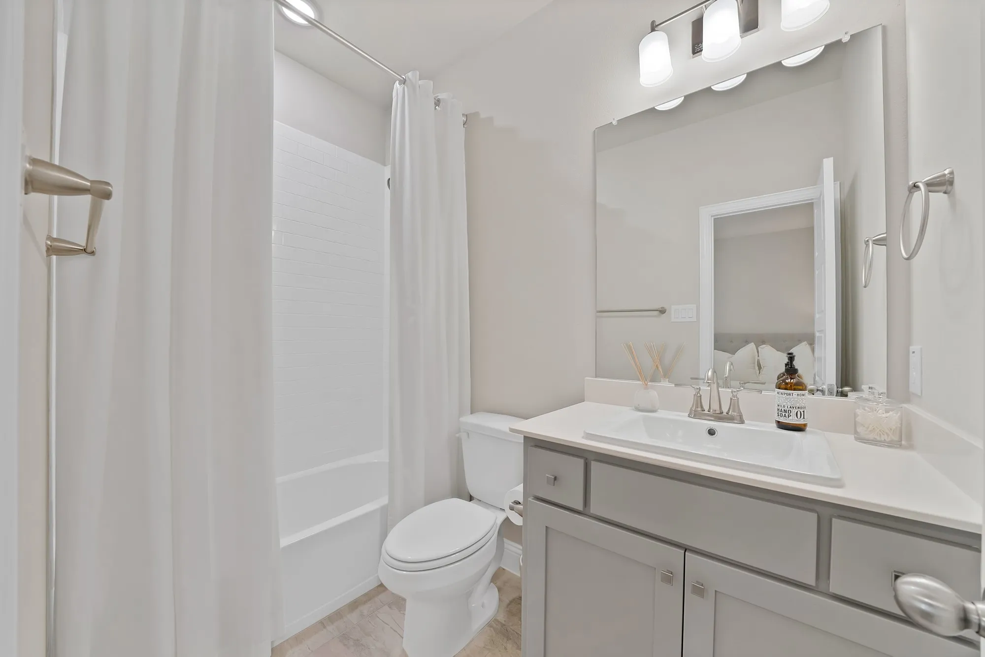 Bathroom featuring a white tub and shower combination, gray vanity with a single basin sink, light-colored countertop, and wall-mounted light fixture