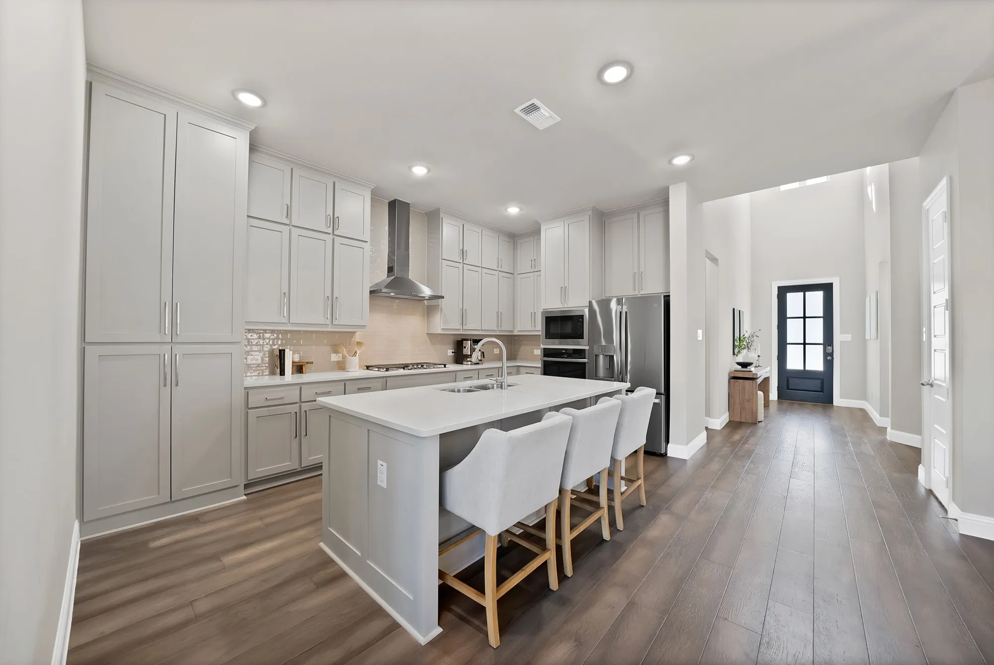 Kitchen featuring extensive light gray cabinetry, a large center island with integrated sink, stainless steel appliances, and wood-finish flooring
