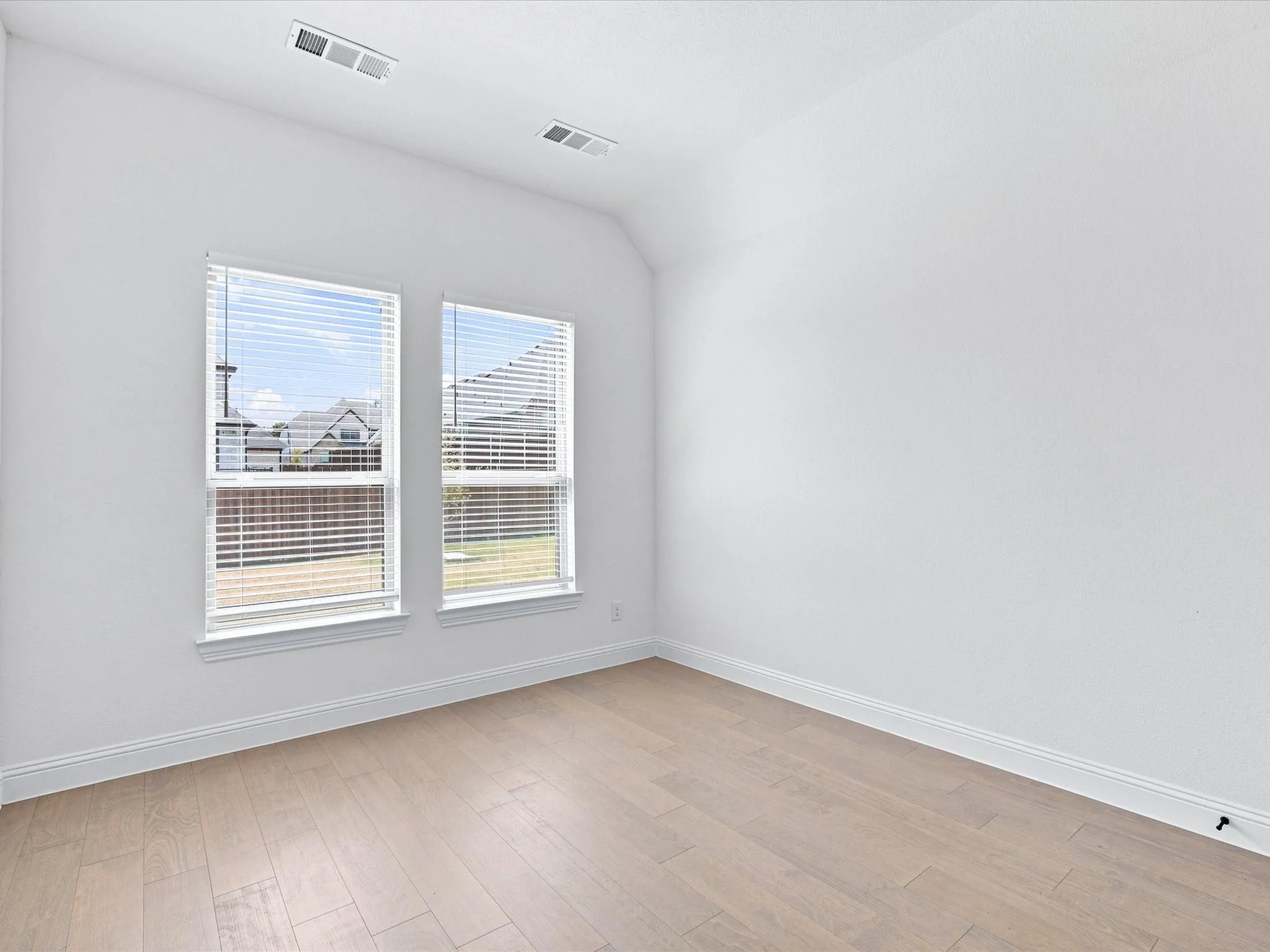 Vaulted ceiling, two windows with blinds, light wood-finish flooring, white walls, and white trim