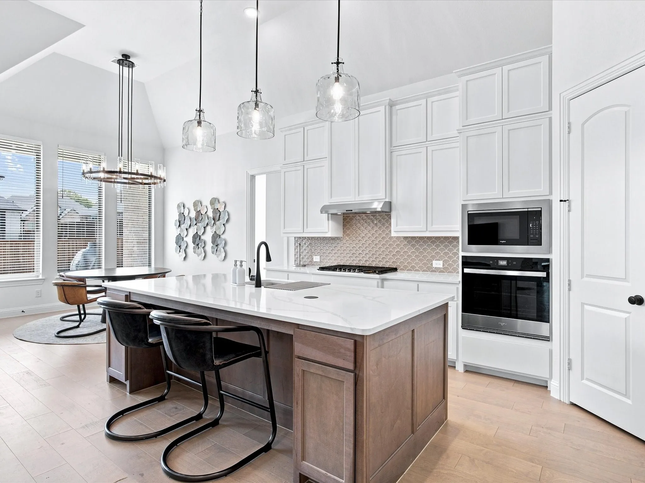 Spacious kitchen featuring an expansive center island with seating, built-in stainless steel appliances, white cabinetry, and light wood-finish flooring