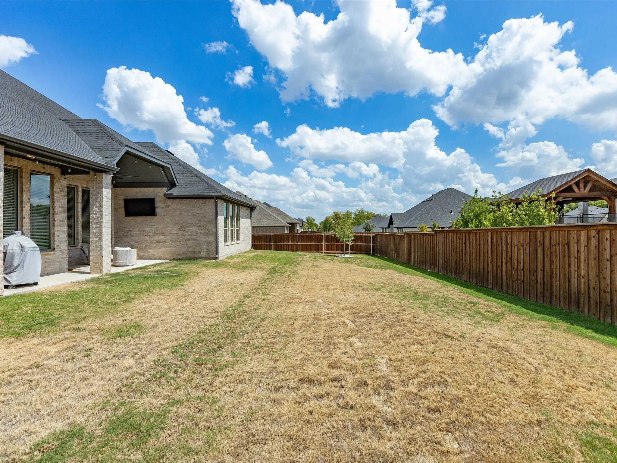 Brick exterior with a covered patio, dark shingle roof, and a wood privacy fence