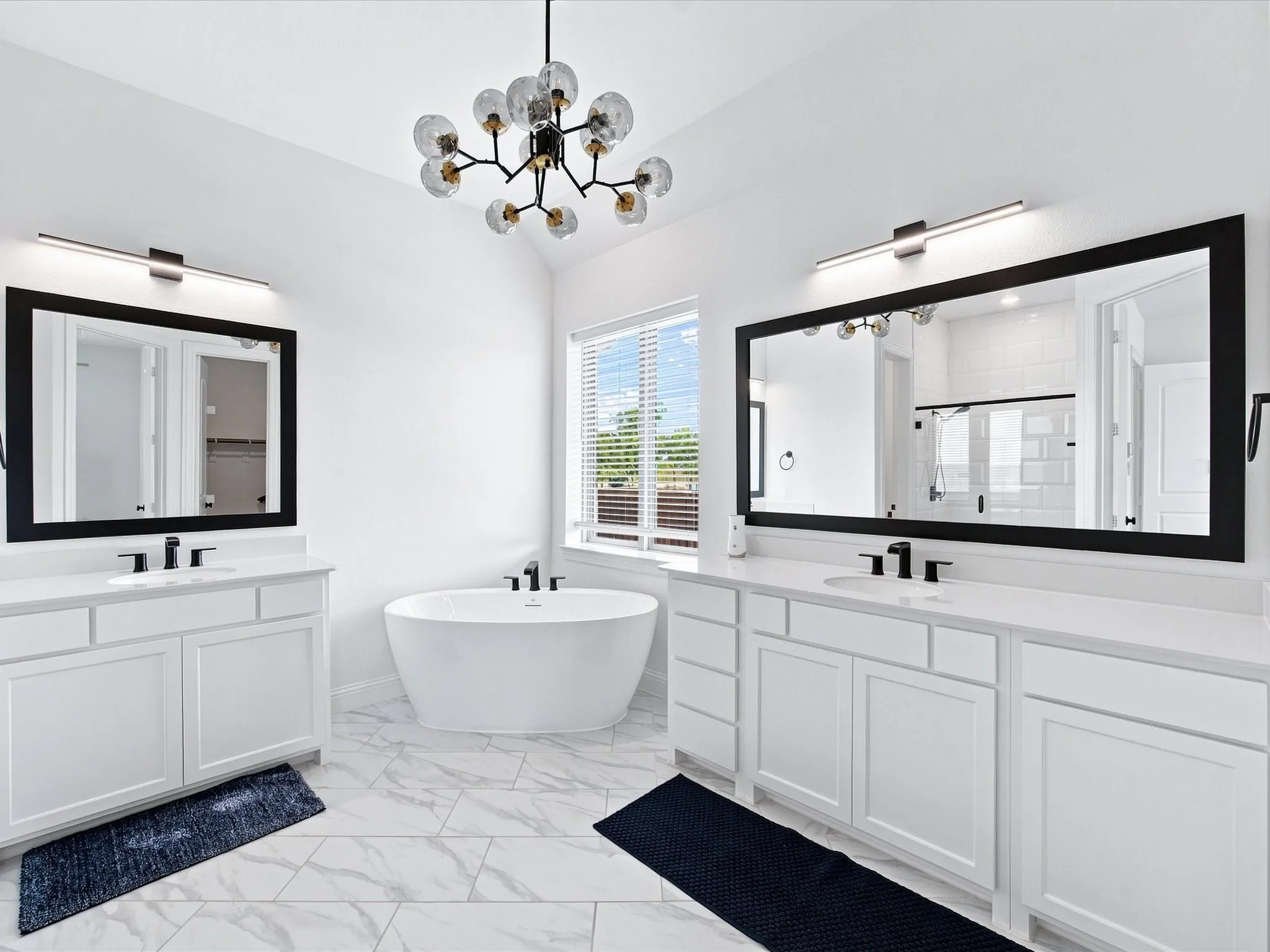 Dual vanity design, freestanding soaking tub, vaulted ceiling, contemporary chandelier, and large framed mirrors
