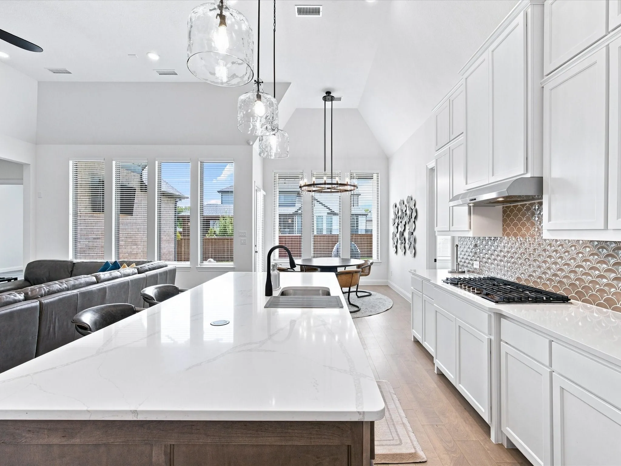 Vaulted ceilings with recessed lighting, large kitchen island with counter seating, gas cooktop, white shaker cabinetry, and a textured backsplash