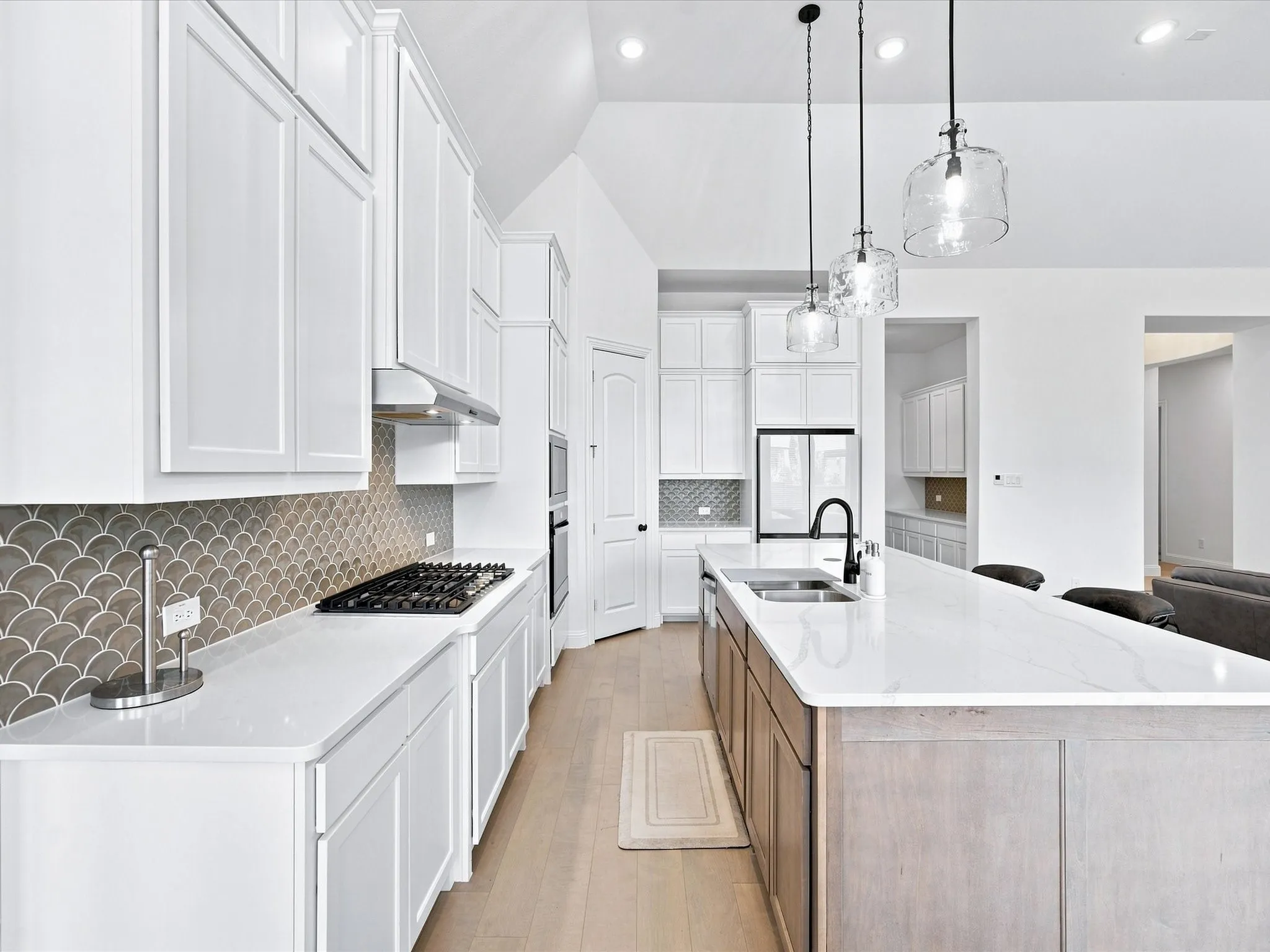 Vaulted ceiling kitchen featuring white cabinetry, a built-in gas range, a white countertop island, and pendant lighting