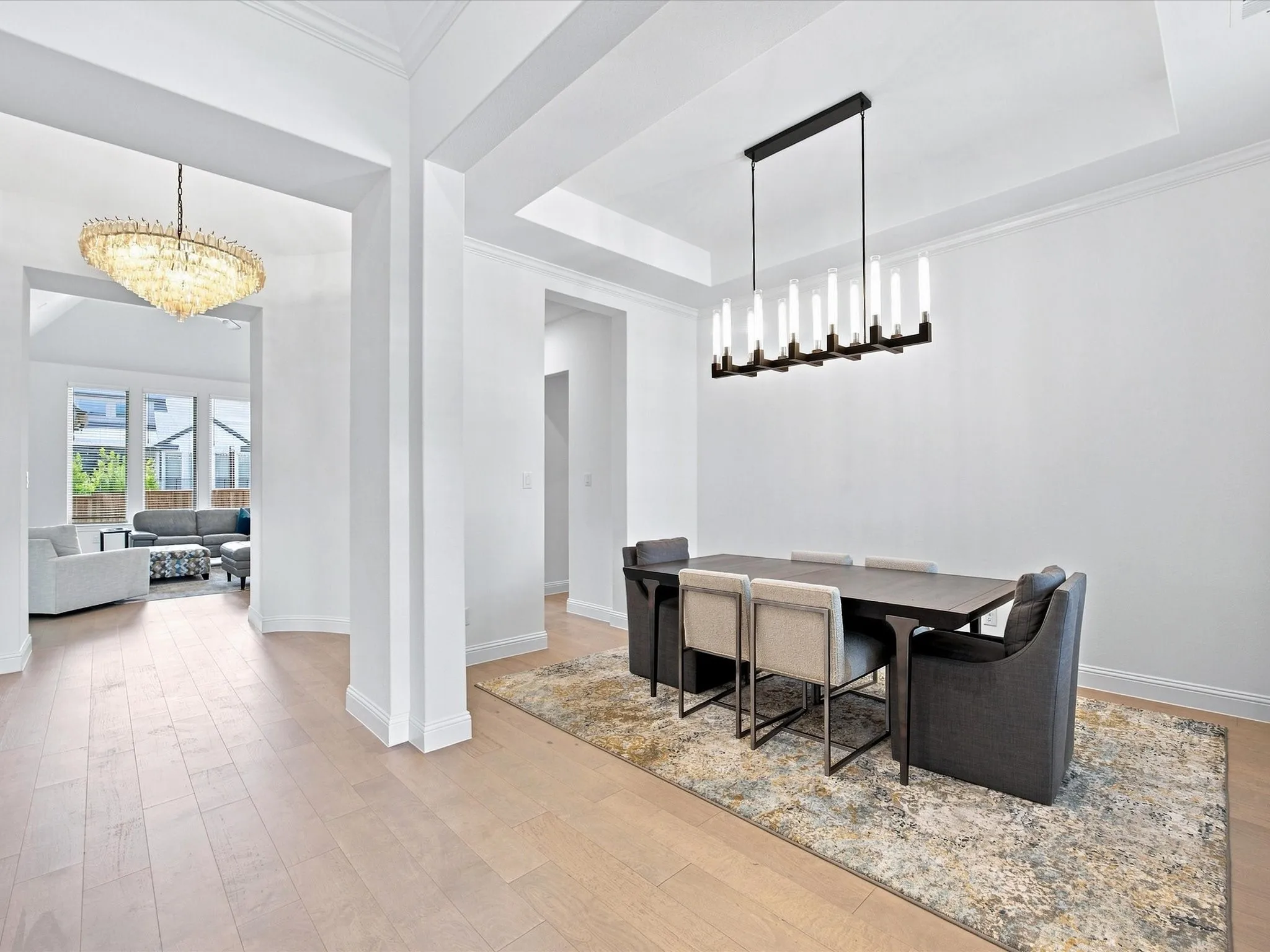 Light wood-finish flooring, recessed ceiling with crown molding, contemporary linear chandelier, arched doorway, and a tray ceiling