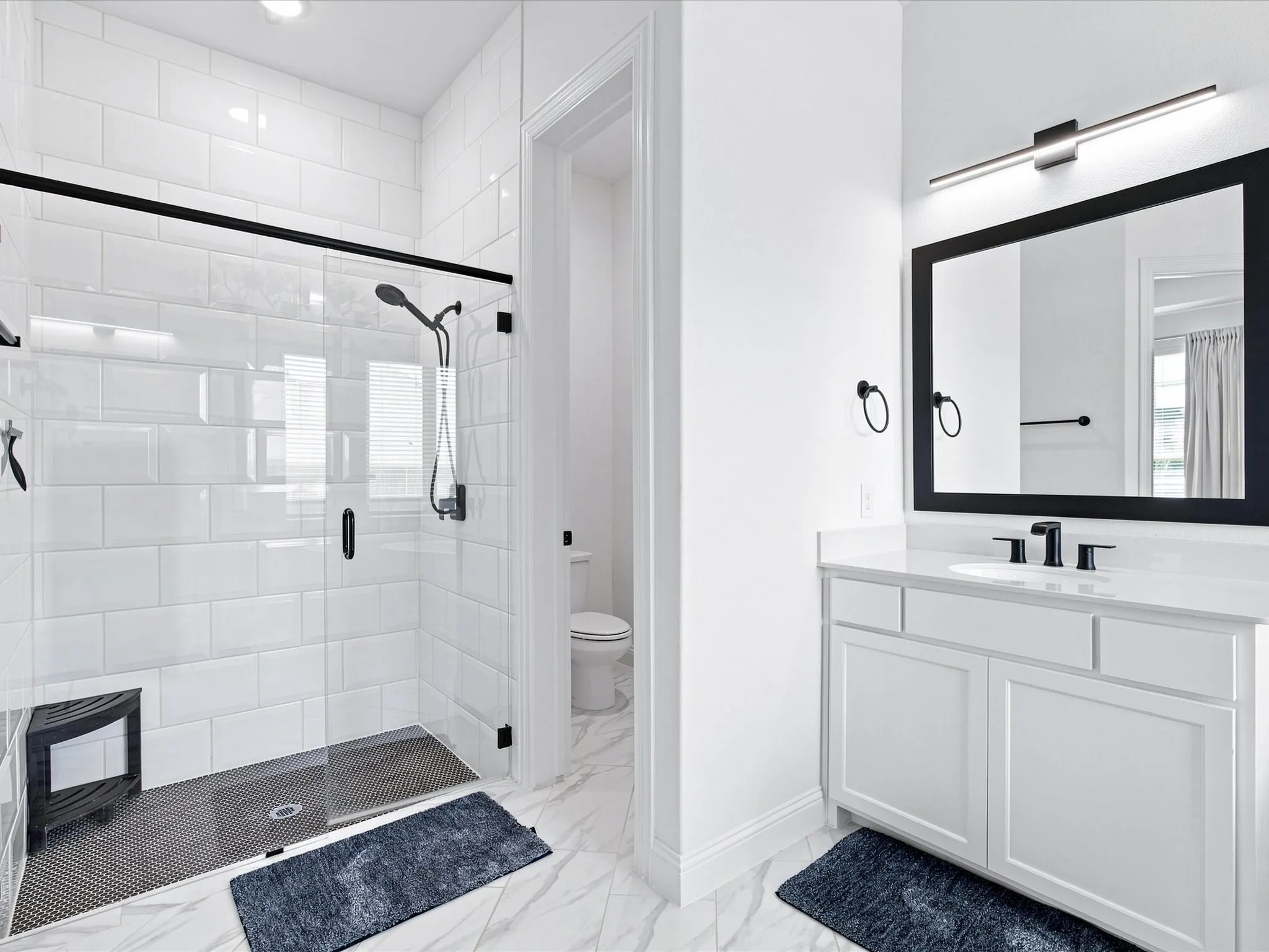 Frameless glass shower with black hardware, white subway tile surround, and a built-in shower bench