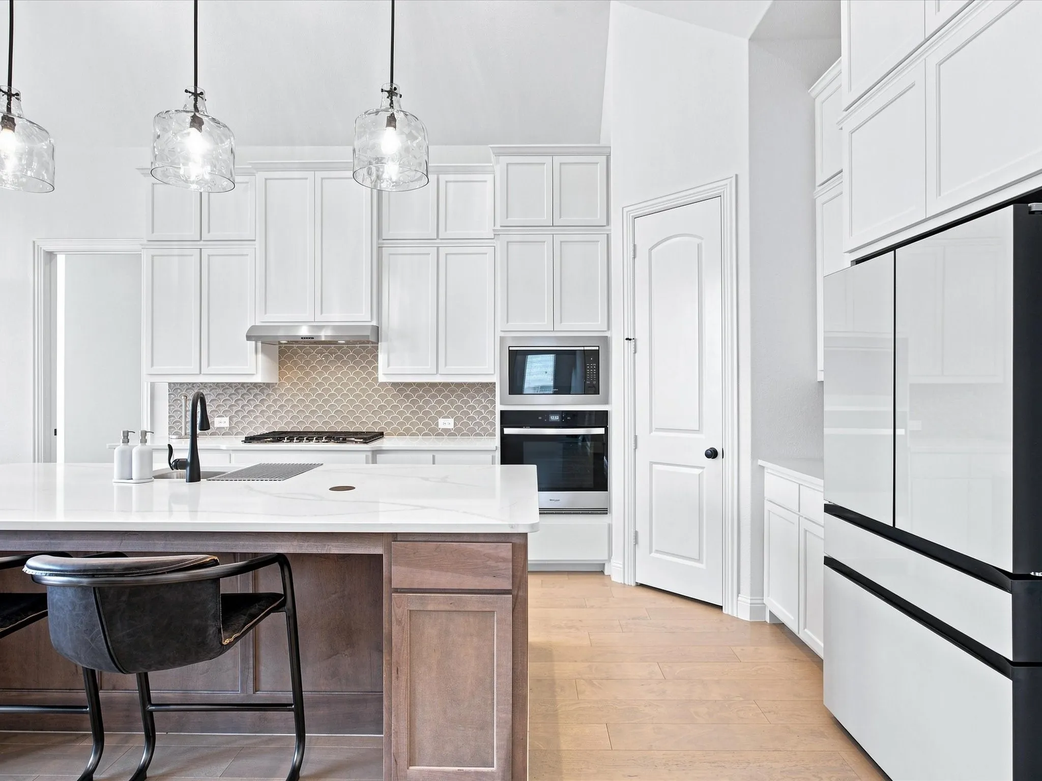 White shaker cabinetry, built-in stainless steel appliances, patterned tile backsplash, wood-finish flooring, and pendant lighting