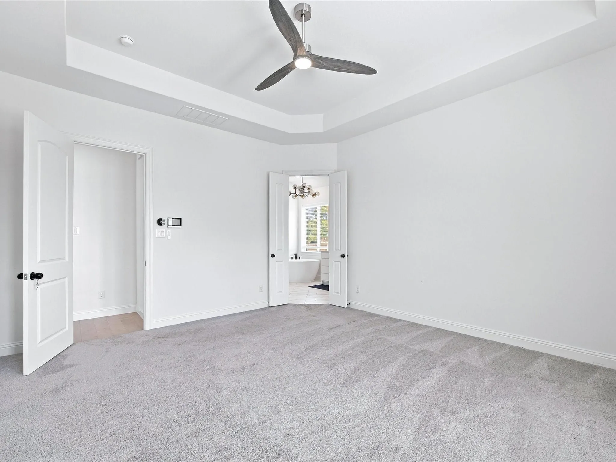 Recessed ceiling with a modern ceiling fan, light gray carpeting, and white paneled doors