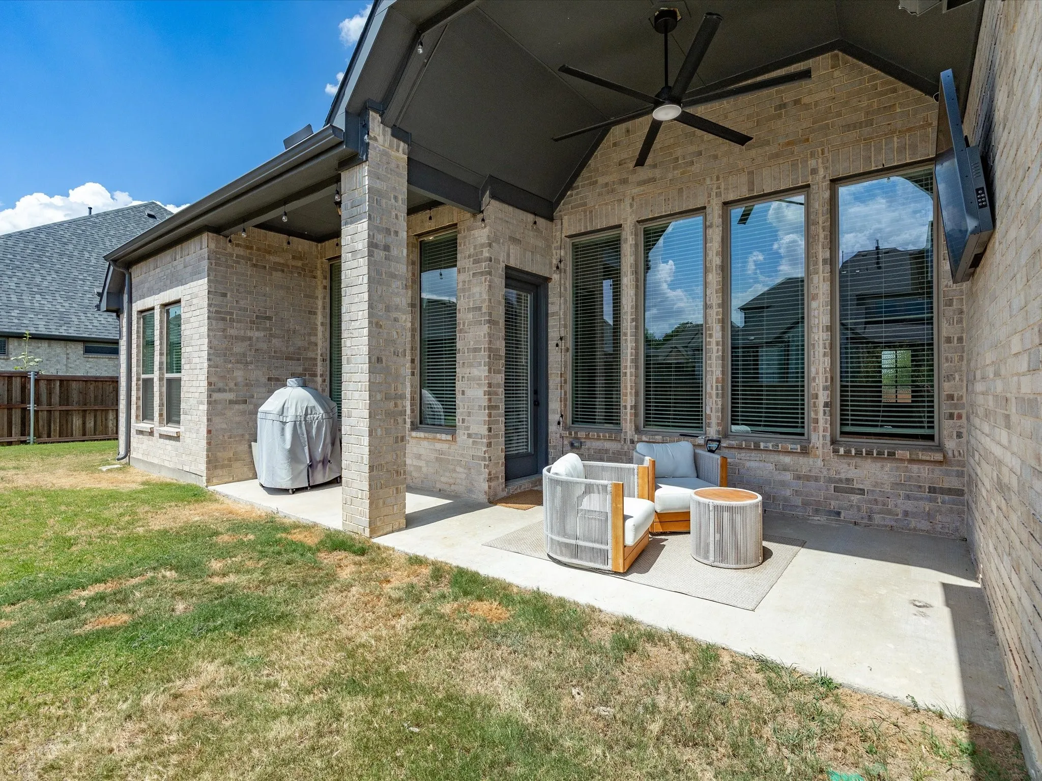 Covered patio featuring a ceiling fan, brick exterior, and multiple large windows