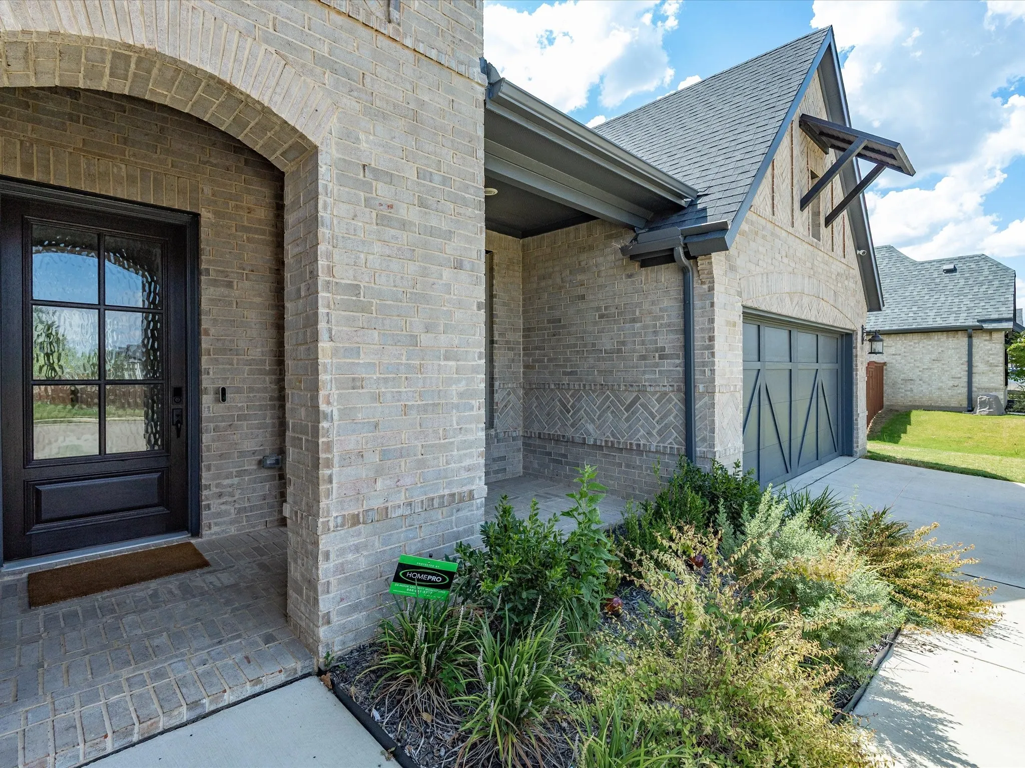 Brick exterior with an arched entryway, decorative glass front door, covered porch, and a two-car garage with an architectural design