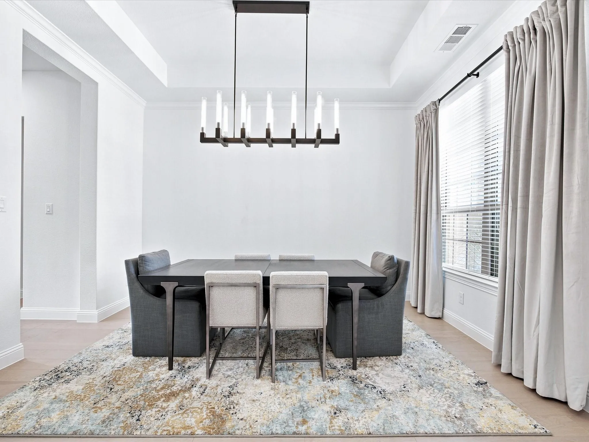 Tray ceiling with crown molding, modern linear chandelier, wood-finish flooring, and a large window with blinds