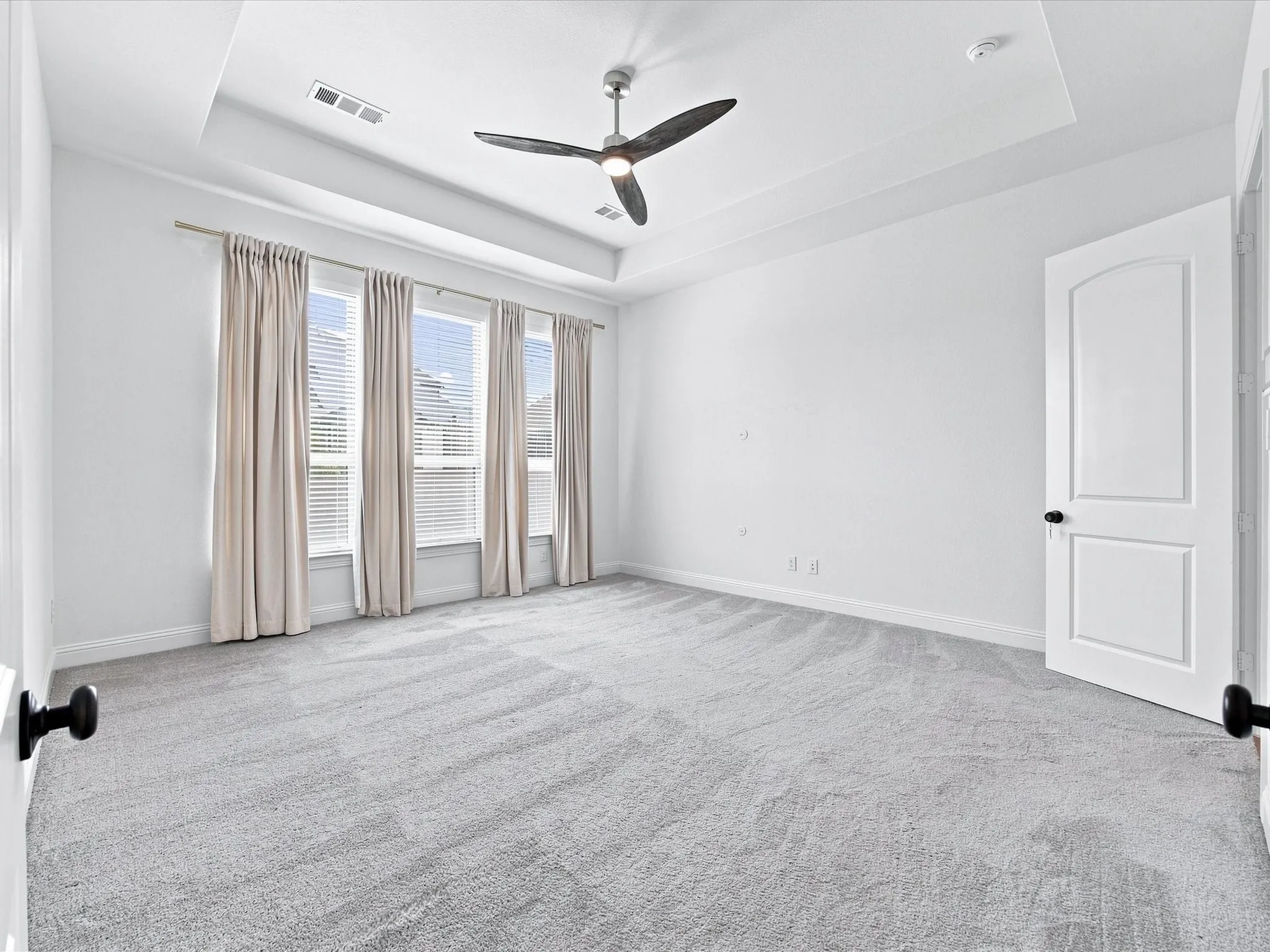 Recessed ceiling with a modern ceiling fan, light gray carpeting, and multiple windows