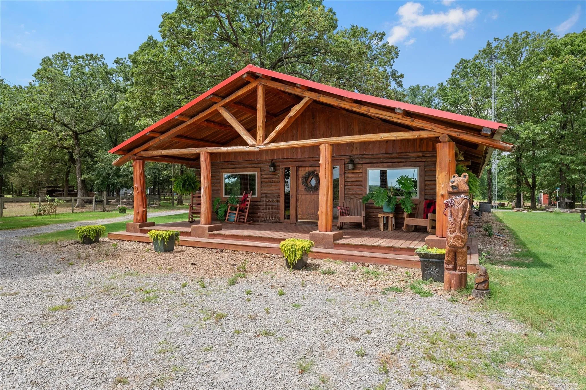 Log cabin exterior with an expansive covered porch, red metal roof, exposed wood beams, and multiple windows.