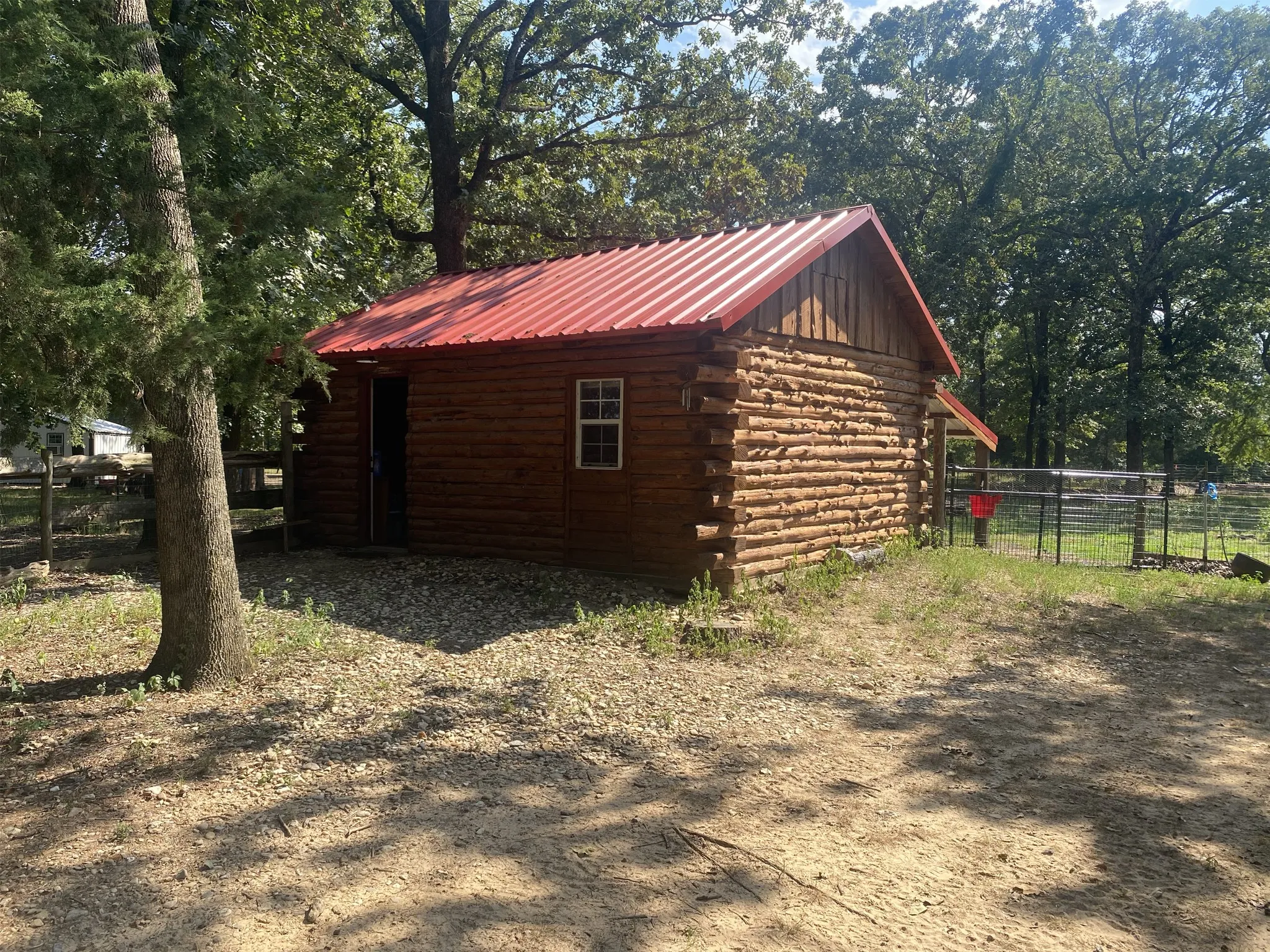 Log cabin structure featuring a red metal roof, a single window, and surrounding trees.