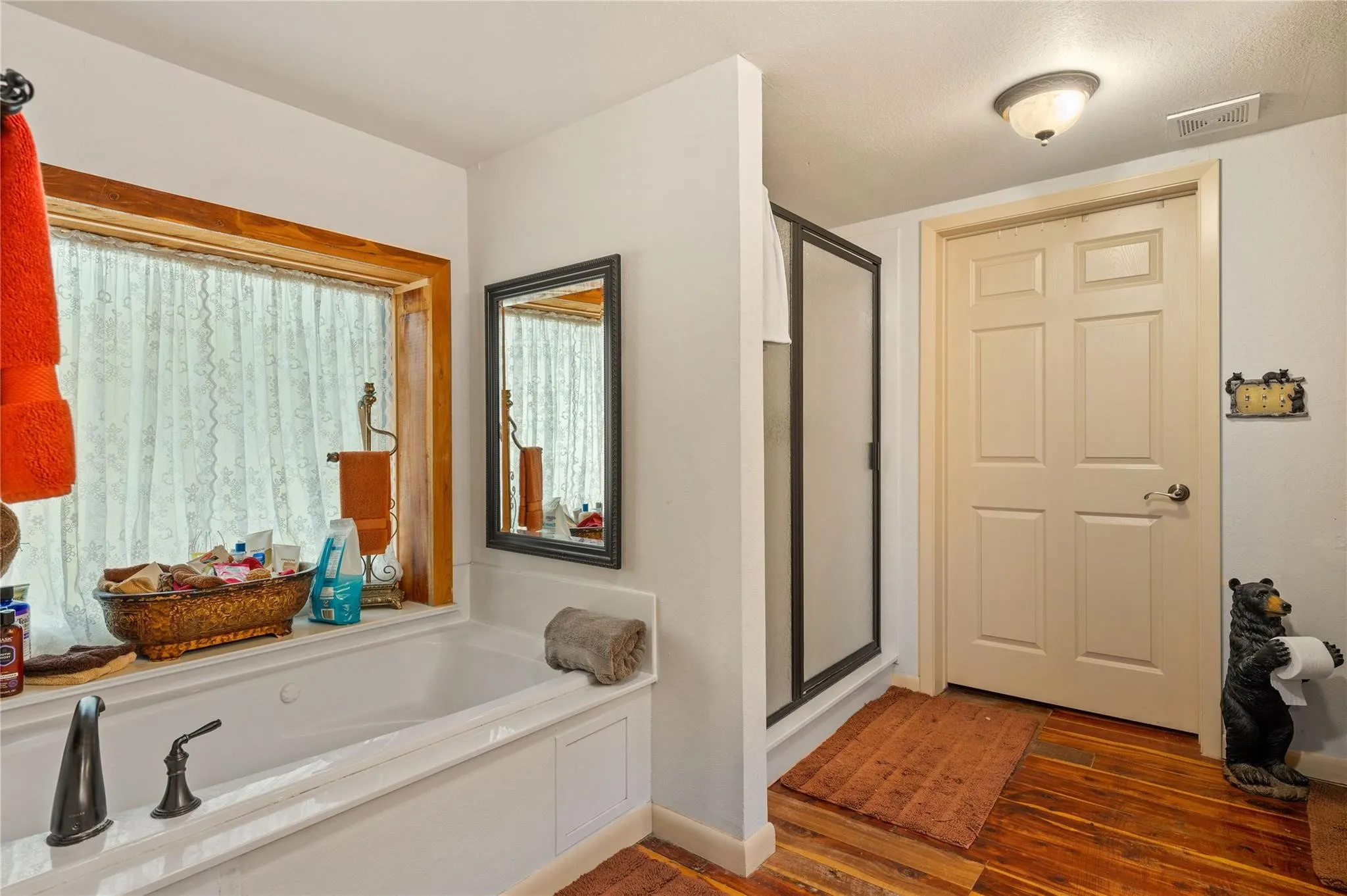 Jetted tub with bronze-tone fixtures, wood-frame window, framed mirror, and a glass-enclosed shower.