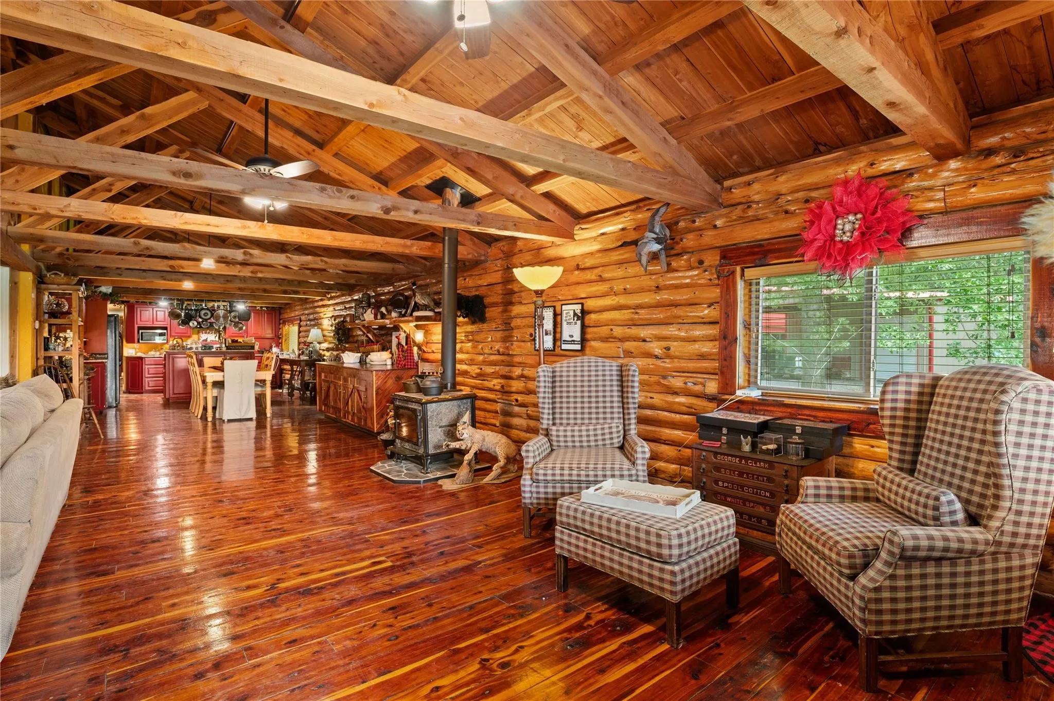 Expansive open-concept living space showcasing exposed timber beam ceiling, gleaming wood-finish flooring throughout, and natural light from large windows.