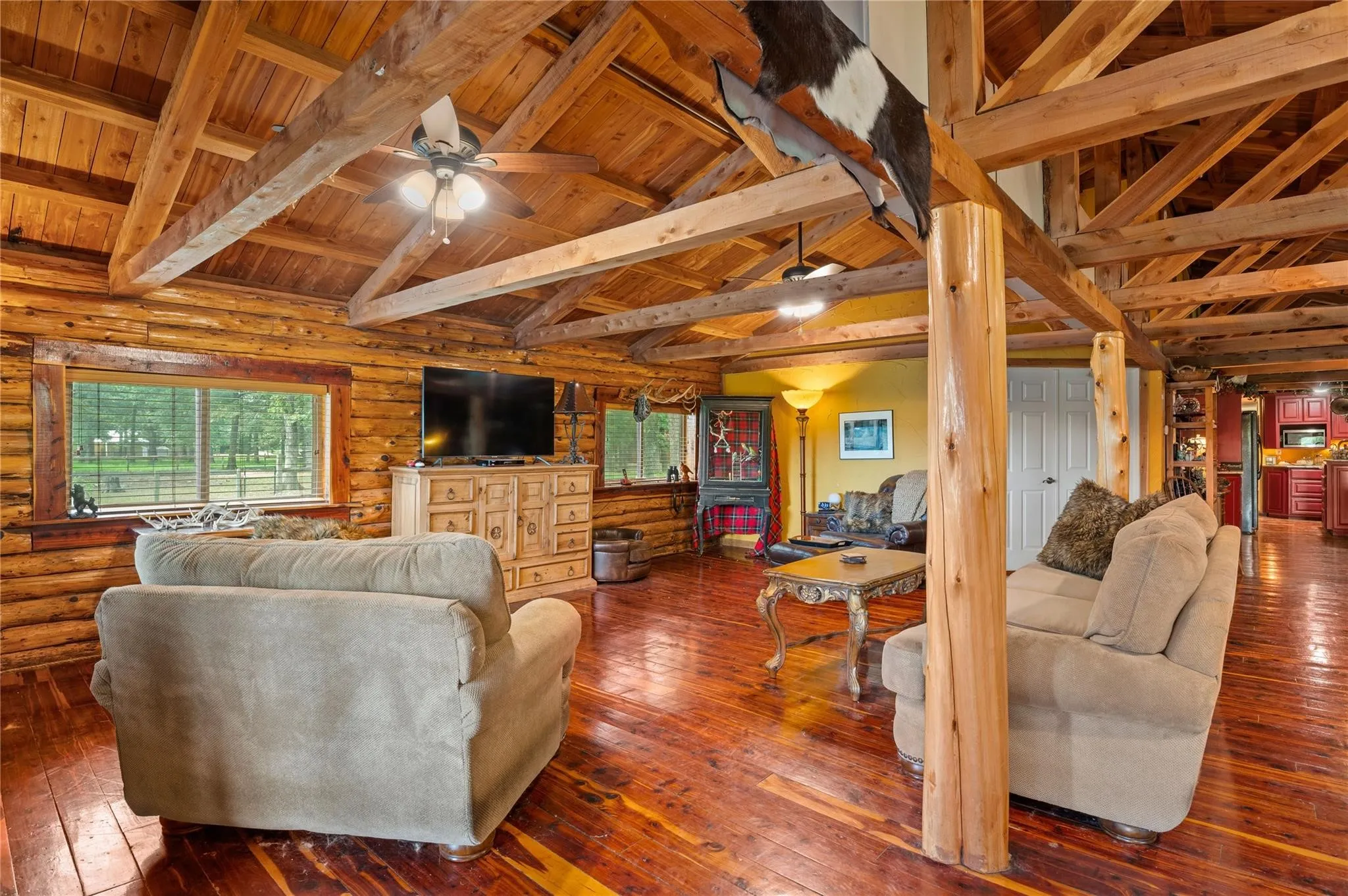 Exposed wood beam ceiling, wood-finish flooring, log wall construction, and a ceiling fan.