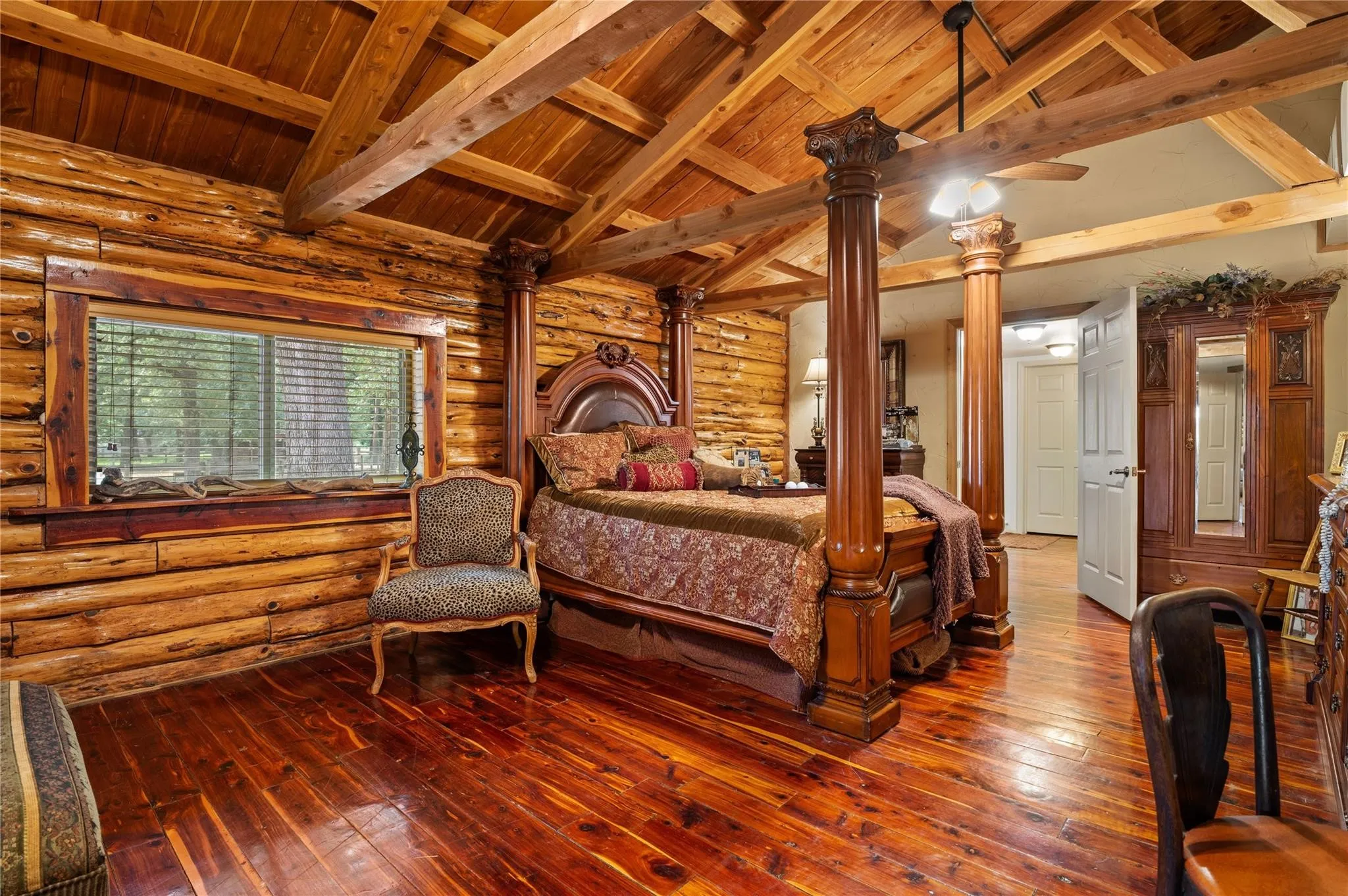 Exposed wood beam ceiling, wood-paneled walls, wood-finish flooring, and a window with blinds.