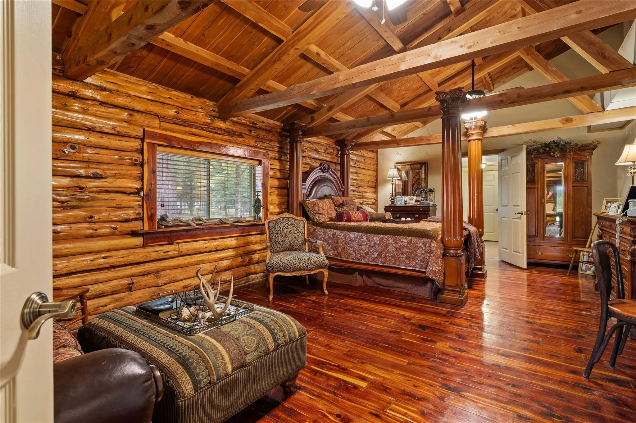 Exposed wood beam ceiling, natural wood log walls, rich wood-finish flooring, and a window with wood trim.