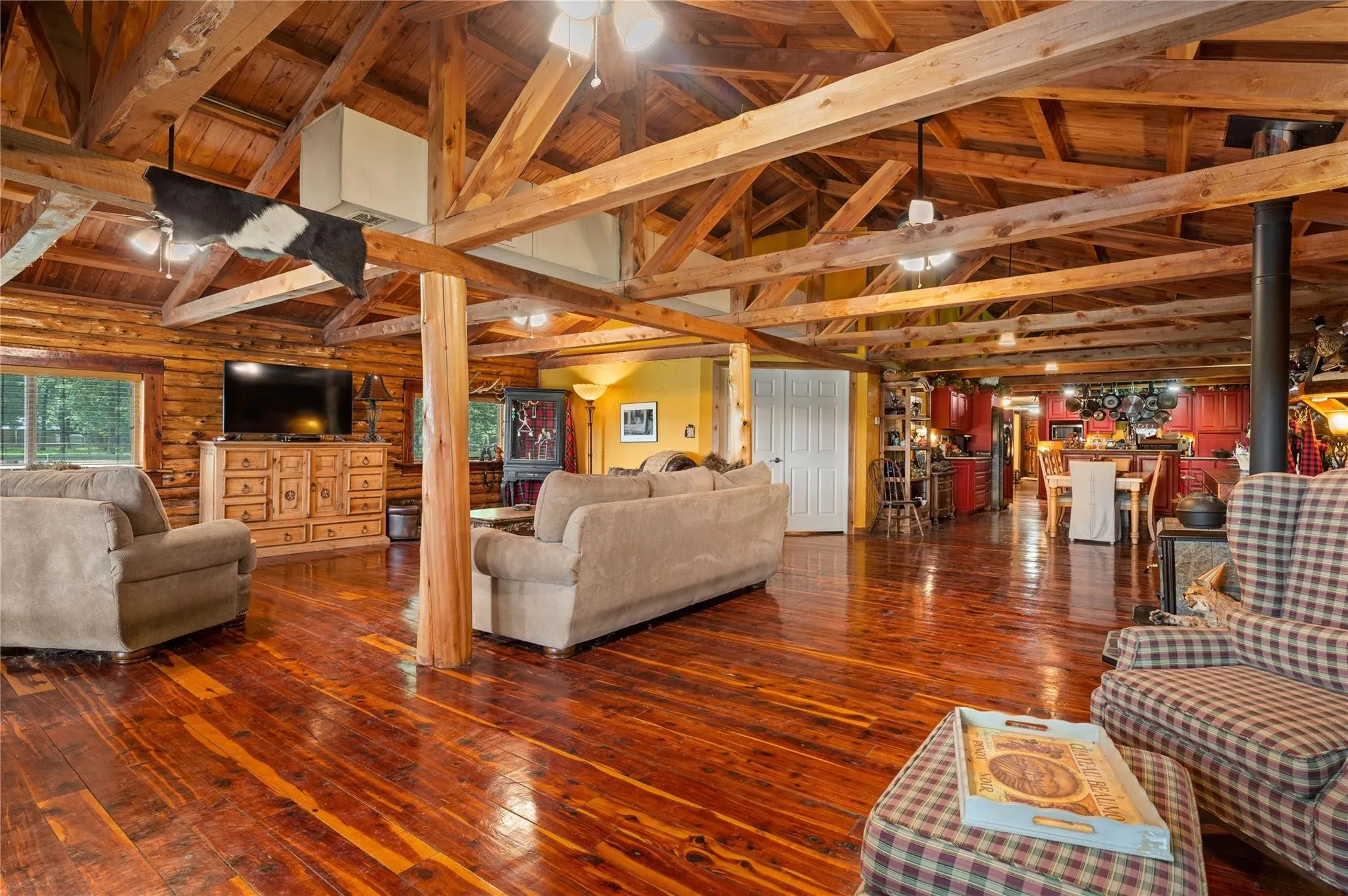 Vaulted ceiling with exposed wood beams, wood-finish flooring, log wall construction, and white paneled door that leads to the Primary bedroom.