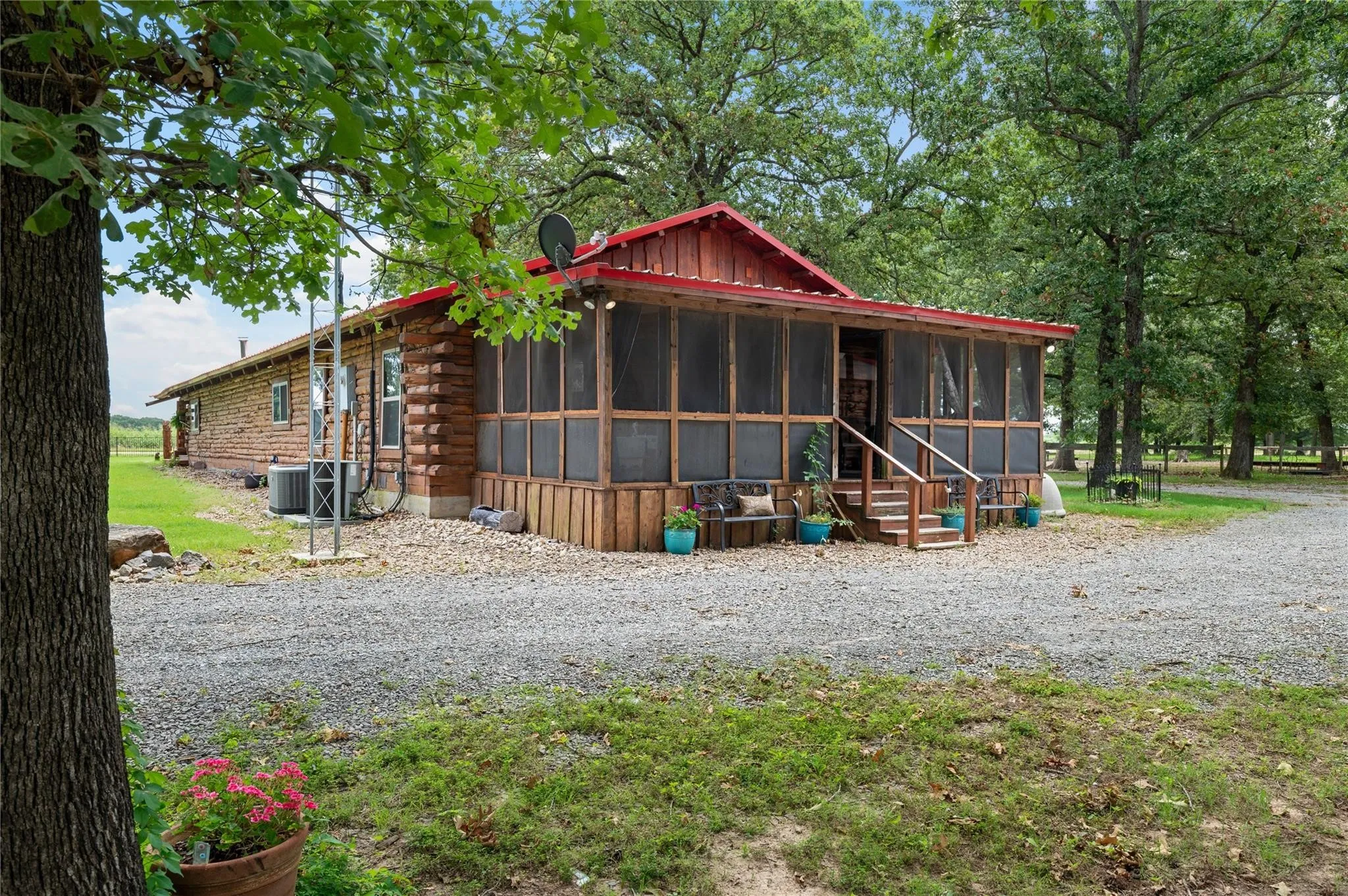 Log cabin exterior with a red metal roof, screened porch, and gravel driveway
