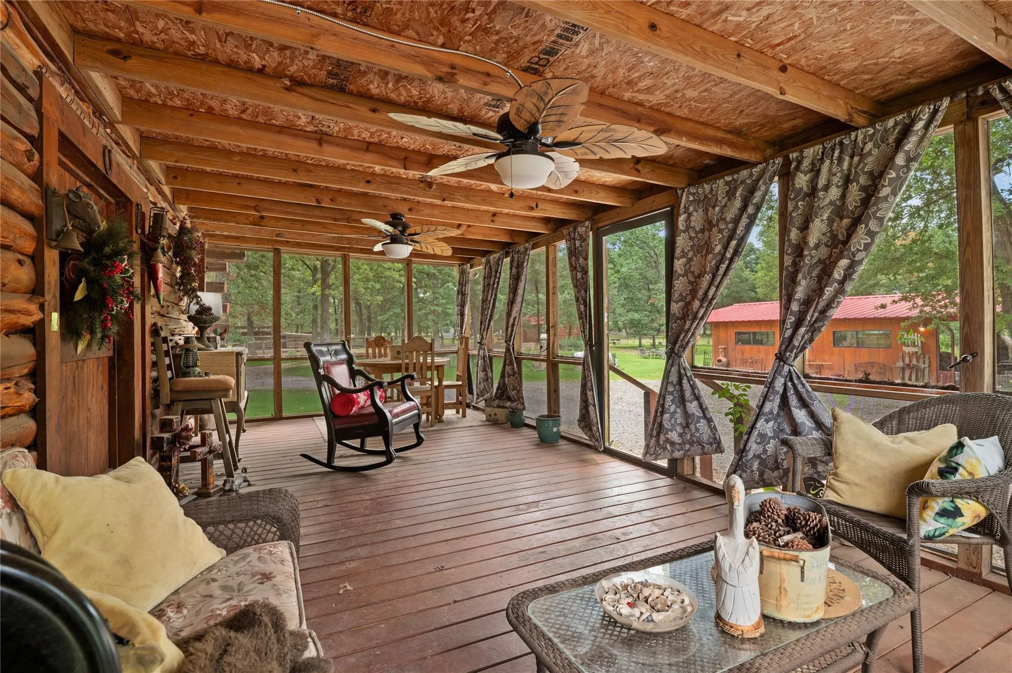 Expansive screened  back porch featuring exposed beam ceiling with ceiling fans, composite wood-finish flooring, and floor-to-ceiling screens with operable curtains for privacy and weather protection.