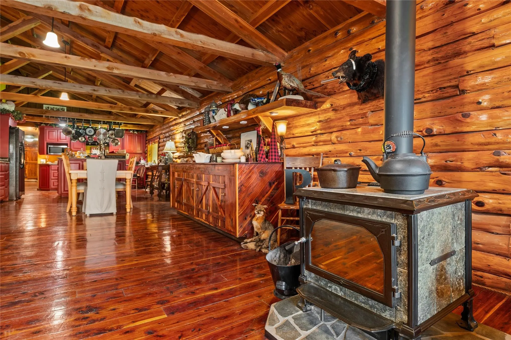 Cedar flooring with exposed wood beam ceiling, wood burning stove, and built in cabinetry.
