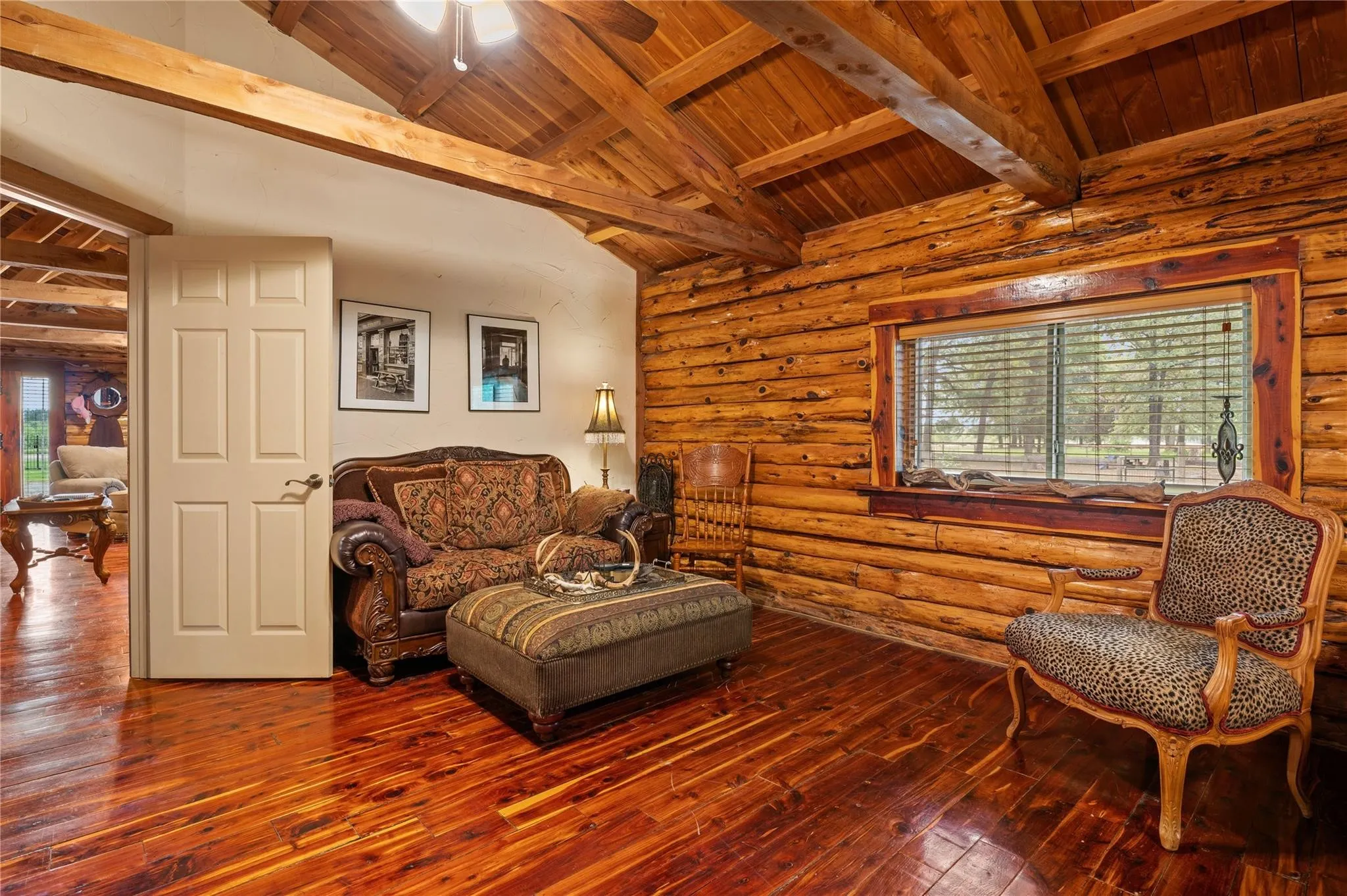Hardwood flooring, exposed wood beam ceiling, wood-paneled walls, built-in window trim, and a six-panel door.