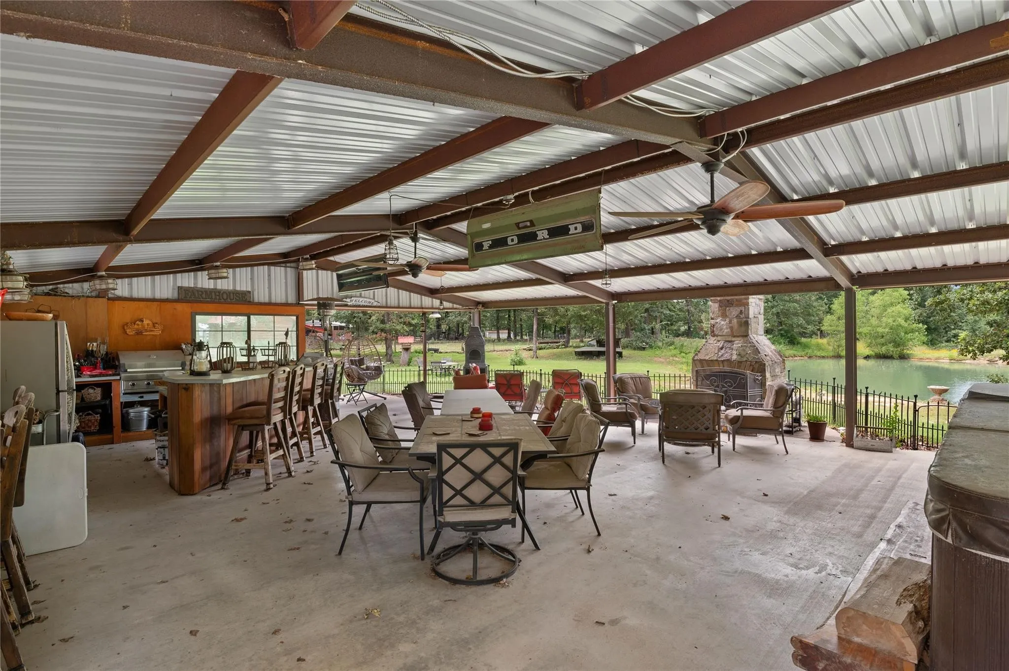 Expansive covered patio featuring a built-in outdoor kitchen with wood-finish cabinetry, a large stone fireplace, pizza oven, grill, bar, refrigerator, and multiple ceiling fans.