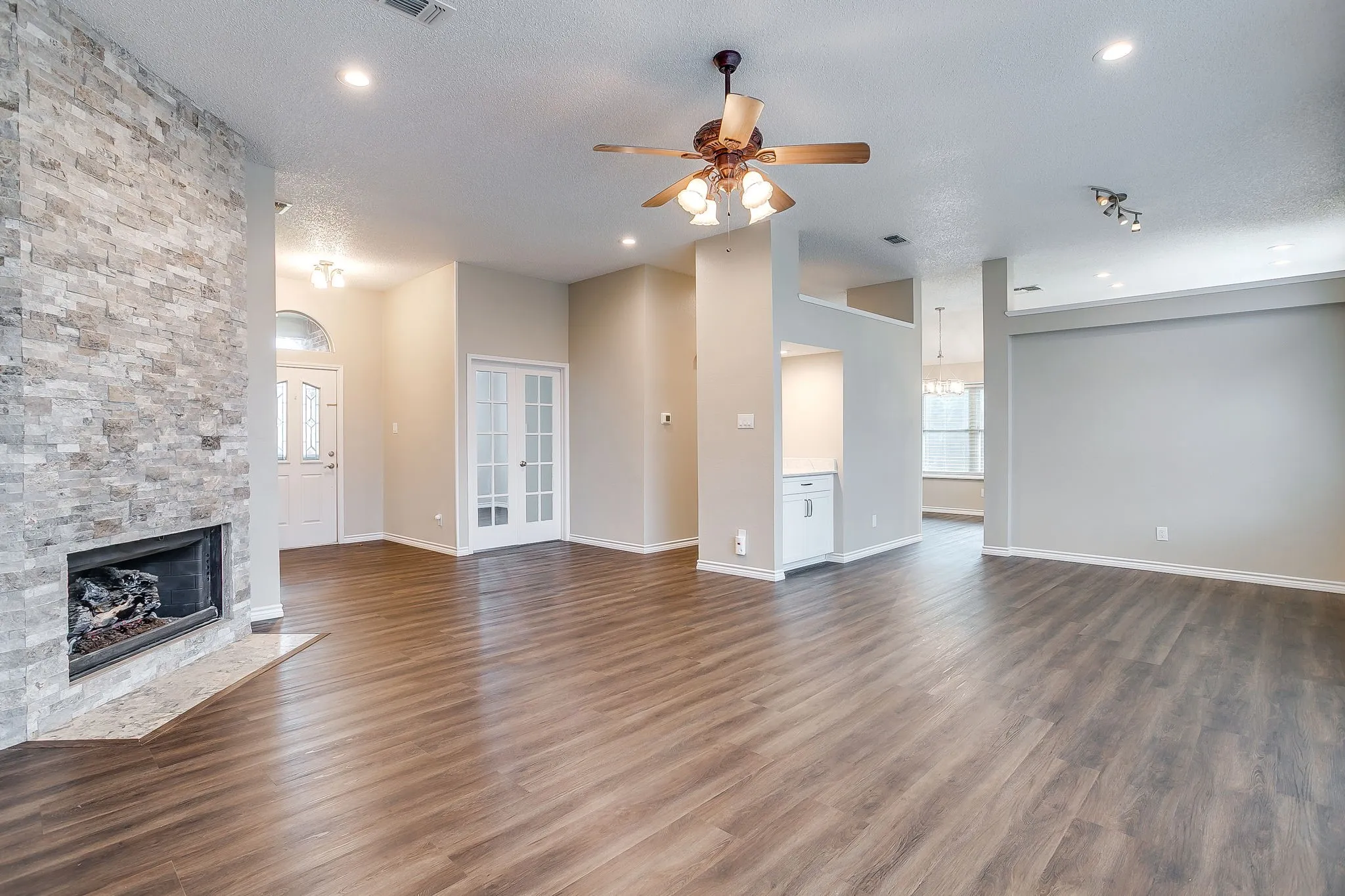 Wood-finish flooring throughout, stone-clad fireplace with hearth, French doors, recessed lighting, and a ceiling fan