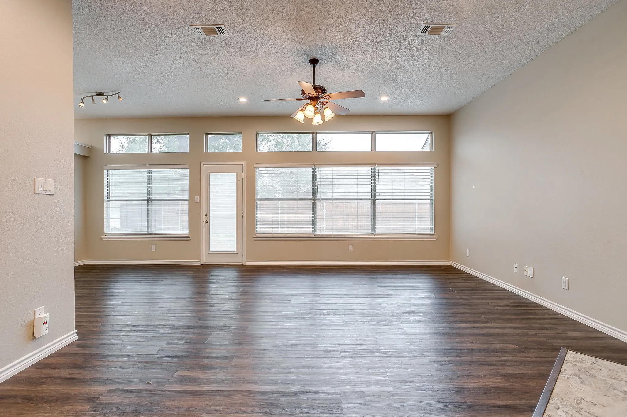 Spacious room featuring wood-finish flooring, high ceilings, a ceiling fan with integrated lighting, and track lighting