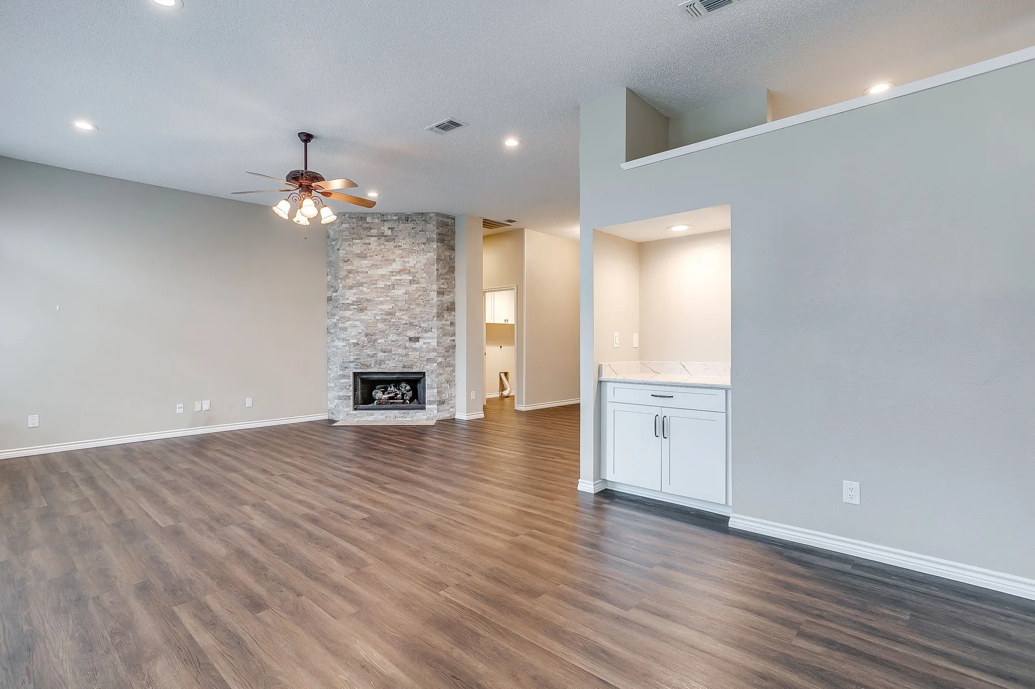Wood-finish flooring, recessed lighting, and a stone-clad fireplace with a hearth