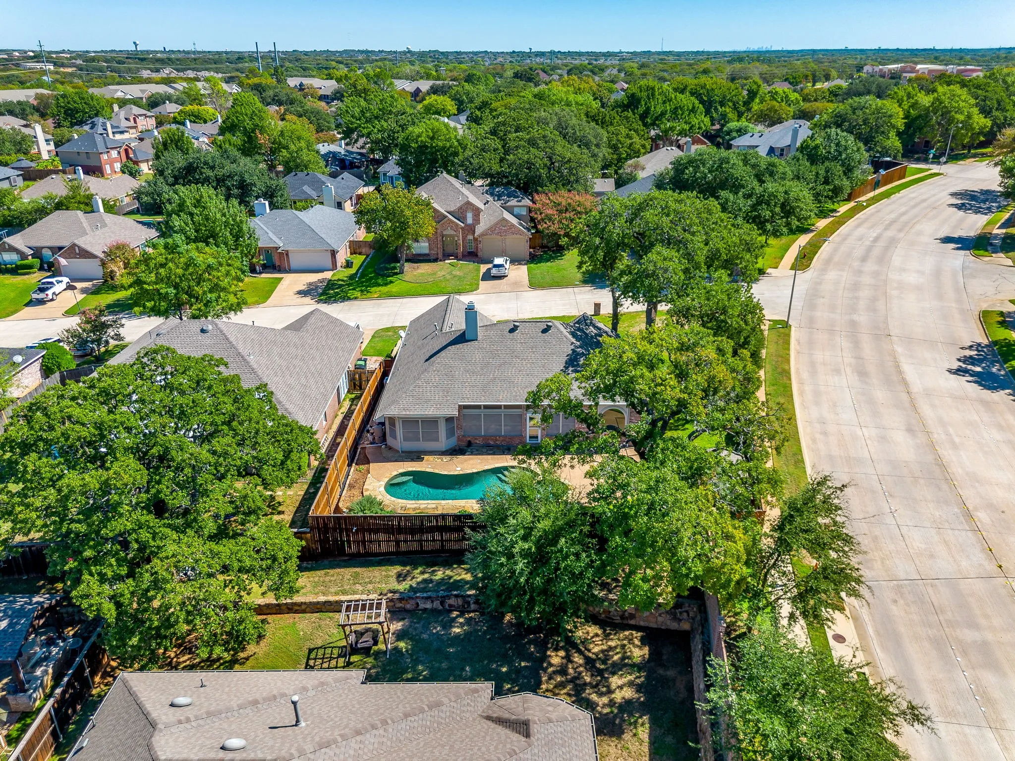 Rear exterior featuring a swimming pool, privacy fencing, and mature trees
